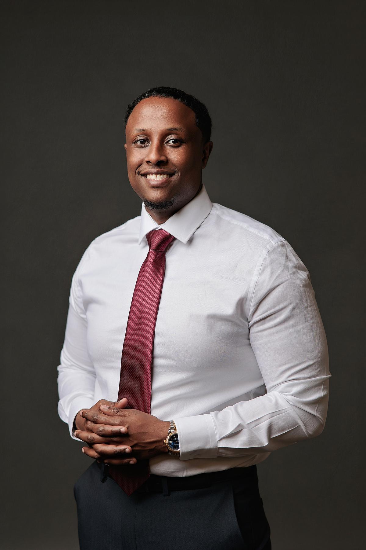 A smiling man in a crisp white shirt and red tie poses for a professional headshot at a Calgary photography studio with soft, studio lighting.