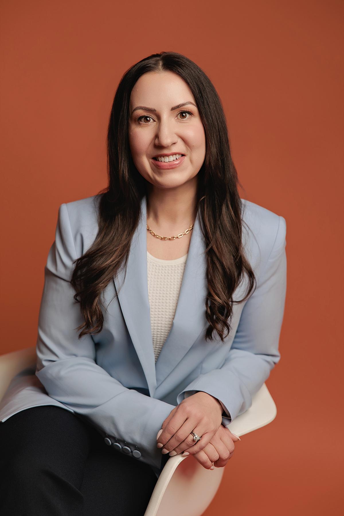 A smiling woman in a light blue blazer poses for a professional headshot at our Calgary photography studio, set against a warm terracotta backdrop.