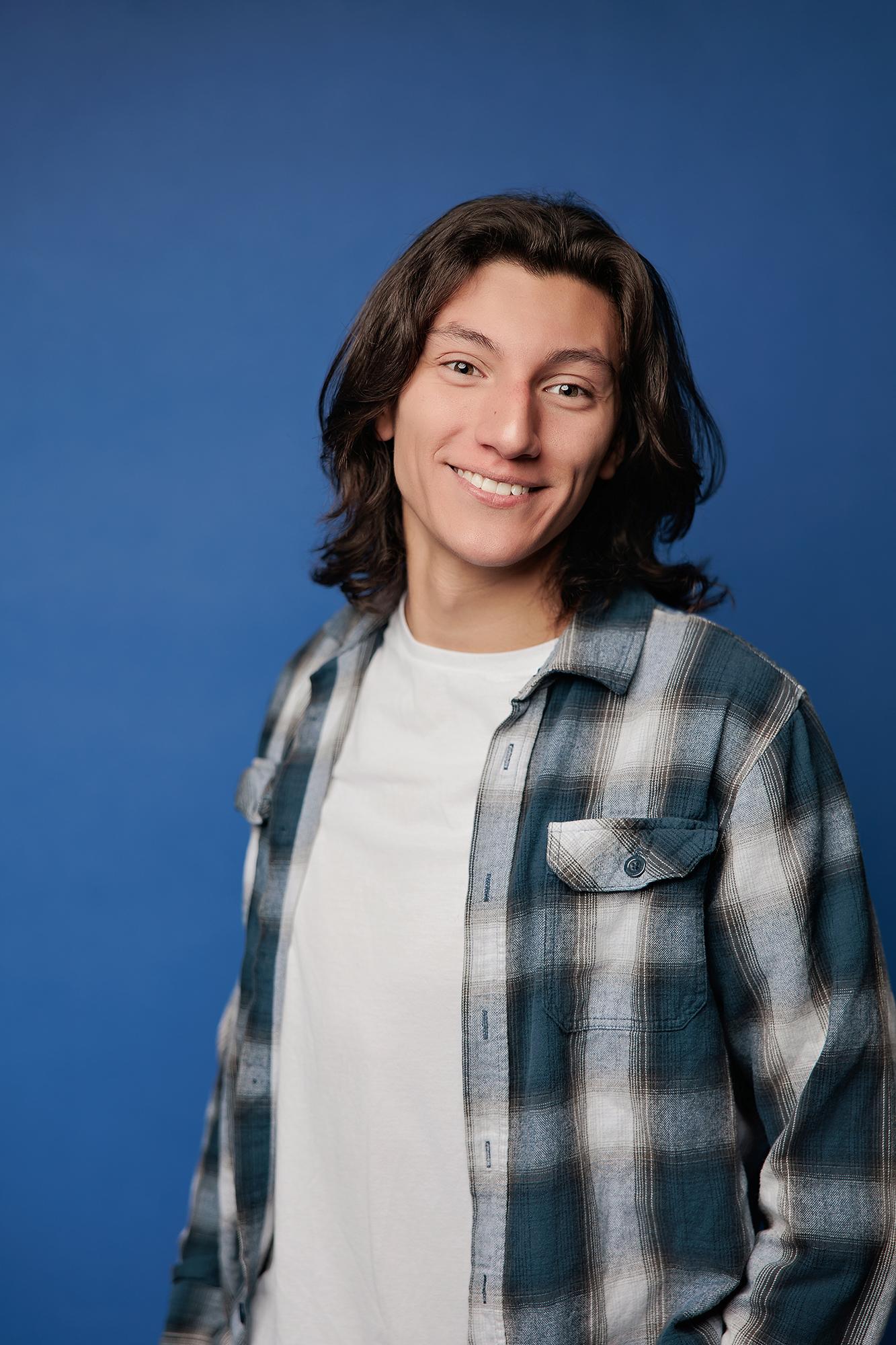 A young man with long dark hair smiles in a plaid shirt at our Calgary photography studio, showcasing the relaxed style of our professional headshots.