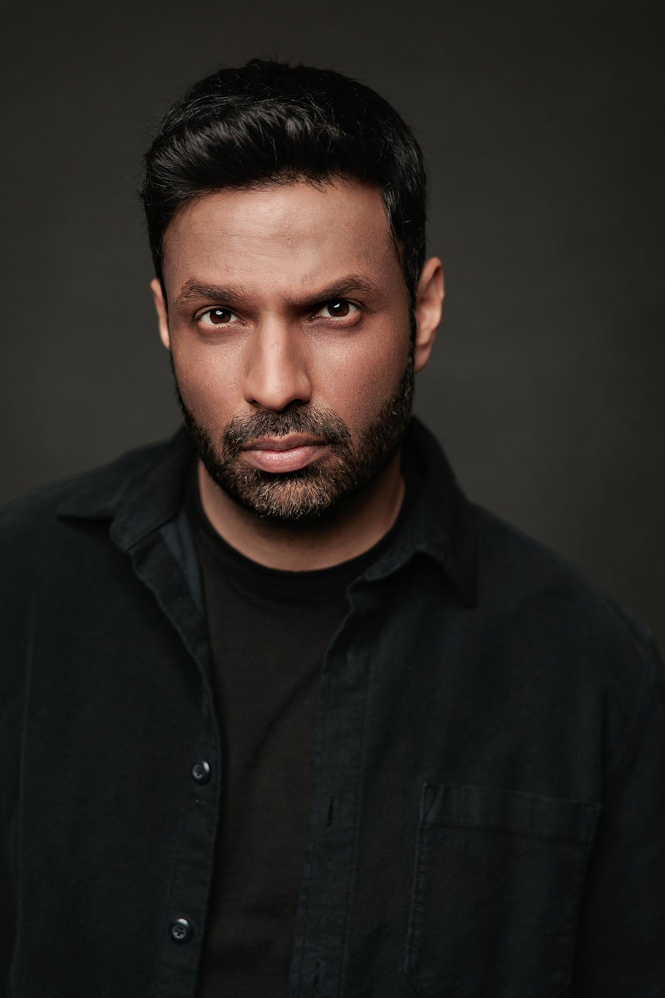 A man with a beard stares intensely in this professional actor headshot captured at a Calgary photography studio, featuring moody lighting and dark attire.