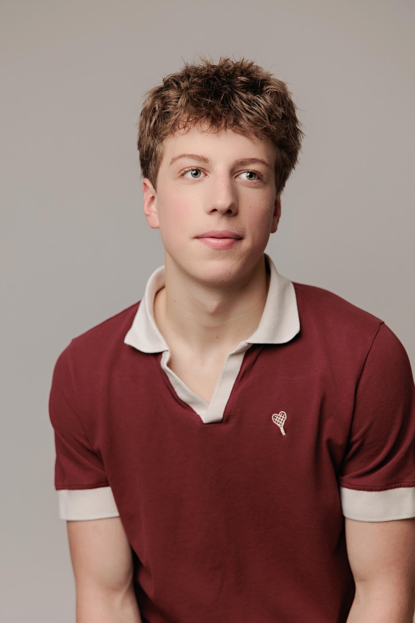 A young actor with textured hair wears a maroon polo shirt in this Calgary actor headshot photography session, captured with soft studio lighting and a neutral backdrop.