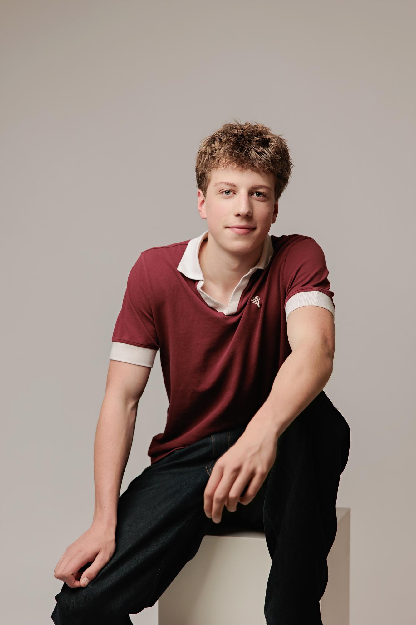 A young actor with messy brown hair wears a maroon polo shirt in this Calgary photography studio portrait, captured with soft lighting for a modern look.