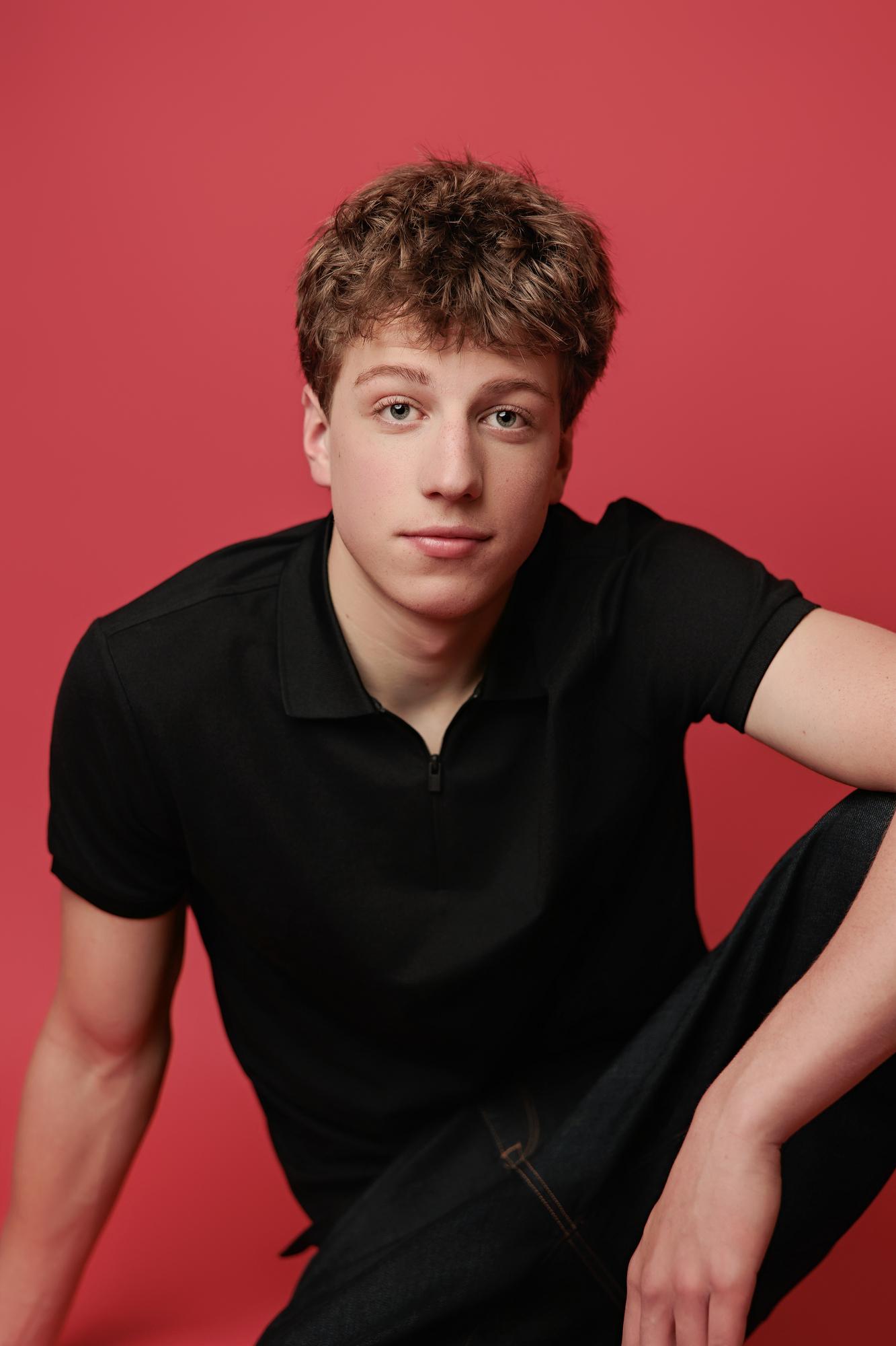 A young actor with textured hair wears a black polo shirt against a vibrant red backdrop, captured by a Calgary professional actor headshot photographer.