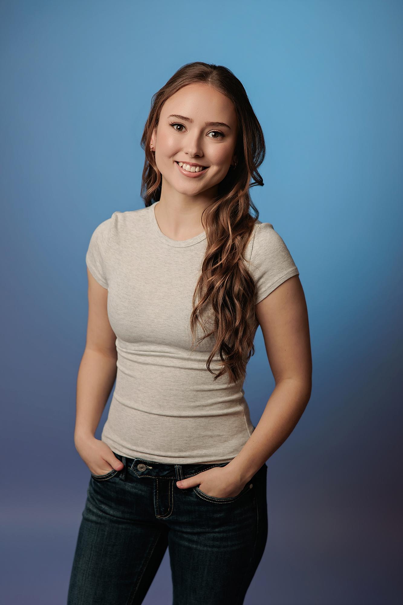 A woman with long wavy hair smiles in a casual grey t-shirt, captured by a Calgary actor headshot photographer using professional studio lighting.