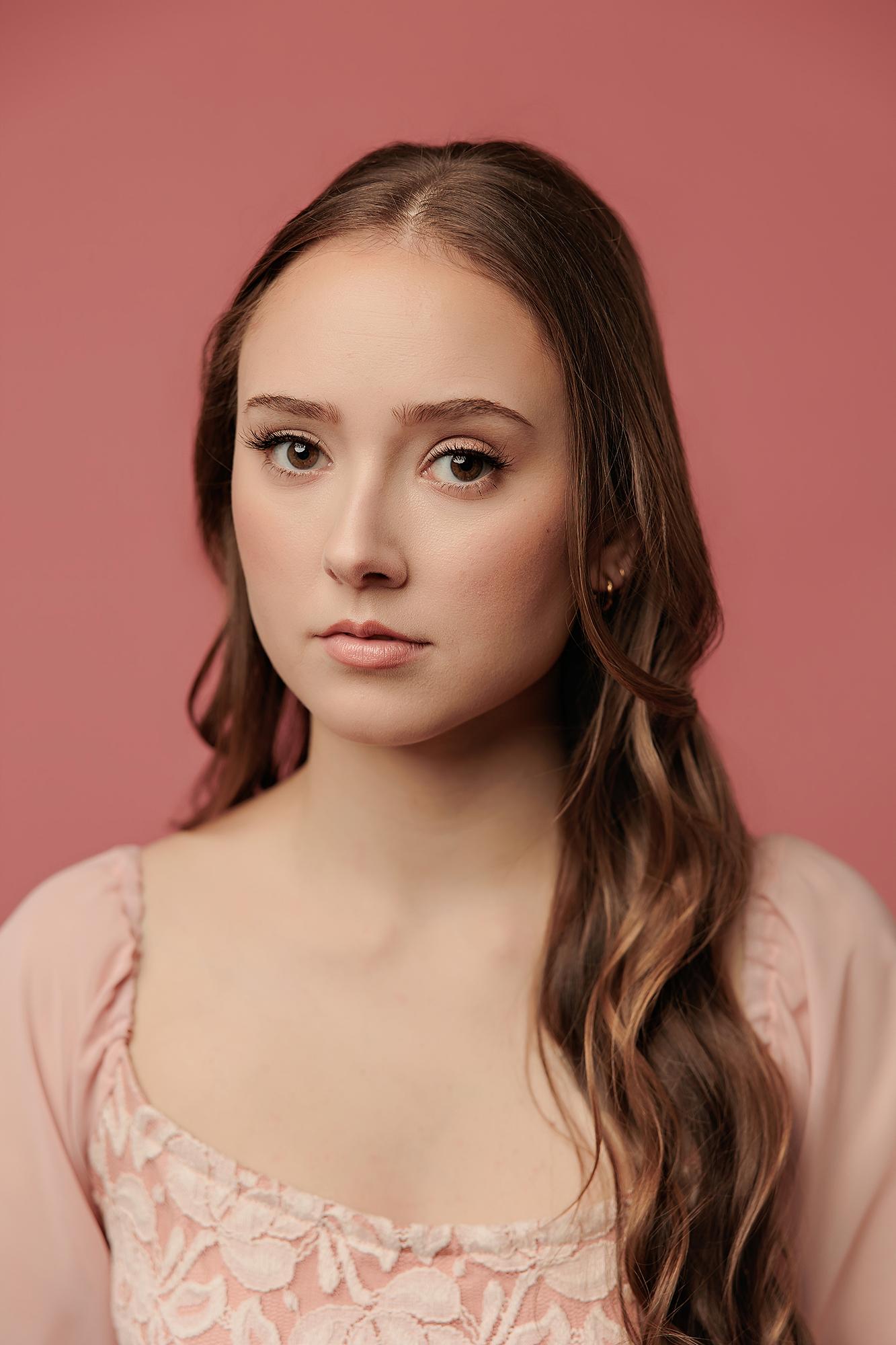 A young actor with long wavy hair poses in a soft pink top against a matching backdrop, showcasing the professional portrait style of our Calgary studio.