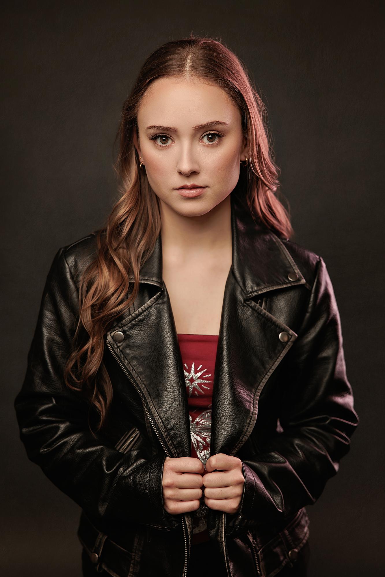 A young woman with long wavy hair wears a leather jacket in this moody Calgary studio portrait, showcasing the professional quality of our headshots.