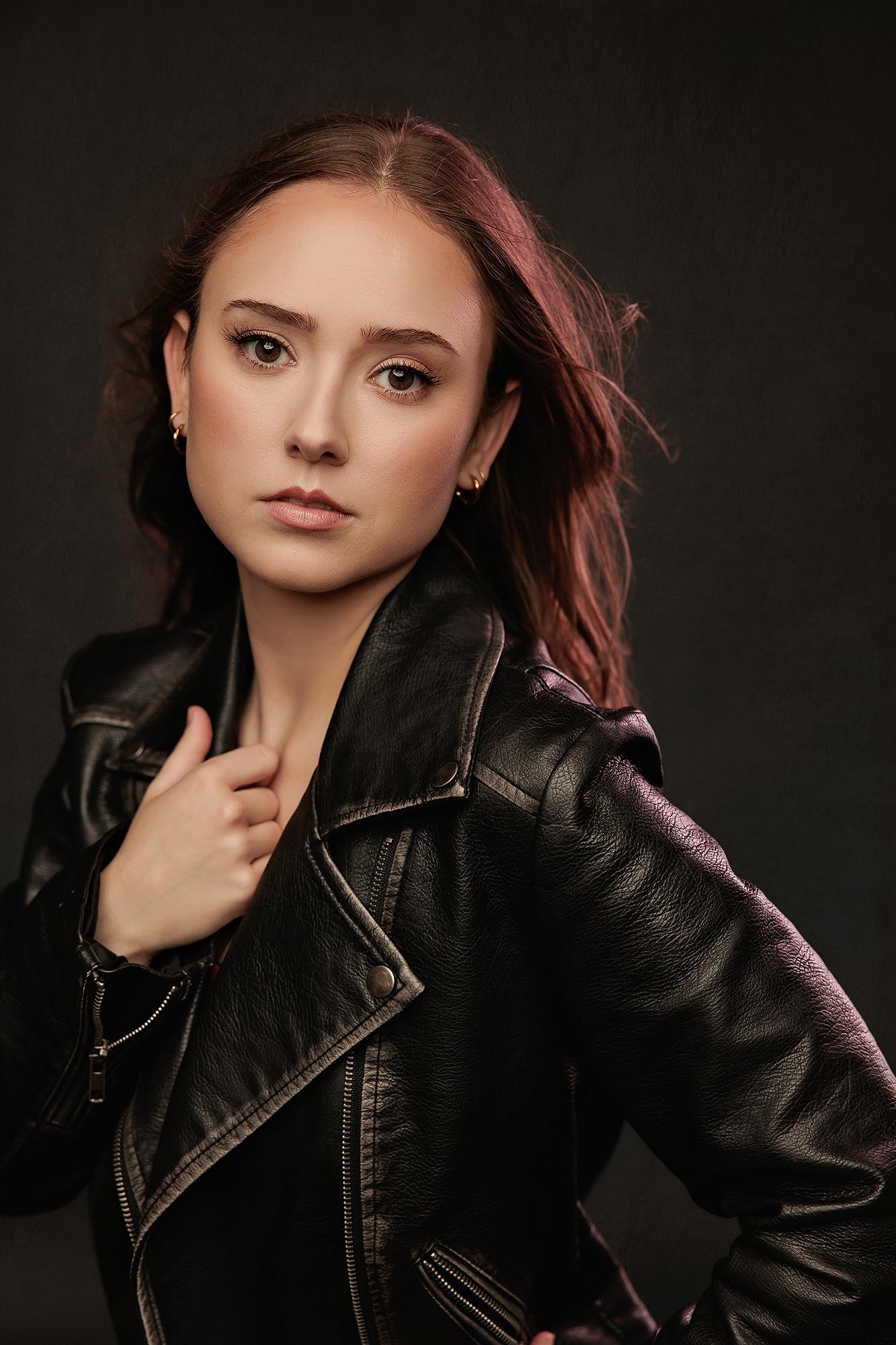A young woman in a leather jacket gazes intently at the camera in this moody portrait captured at our professional Calgary photography studio.