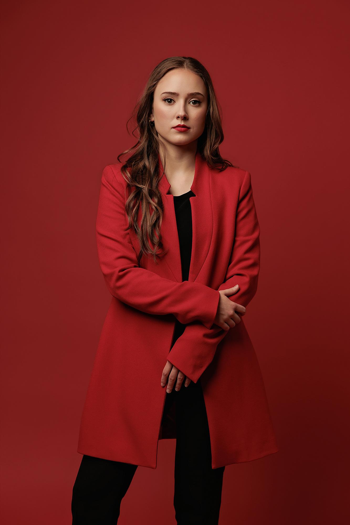 A woman with long wavy hair wears a red blazer in this Calgary photography studio portrait, featuring bold lighting against a matching red backdrop.