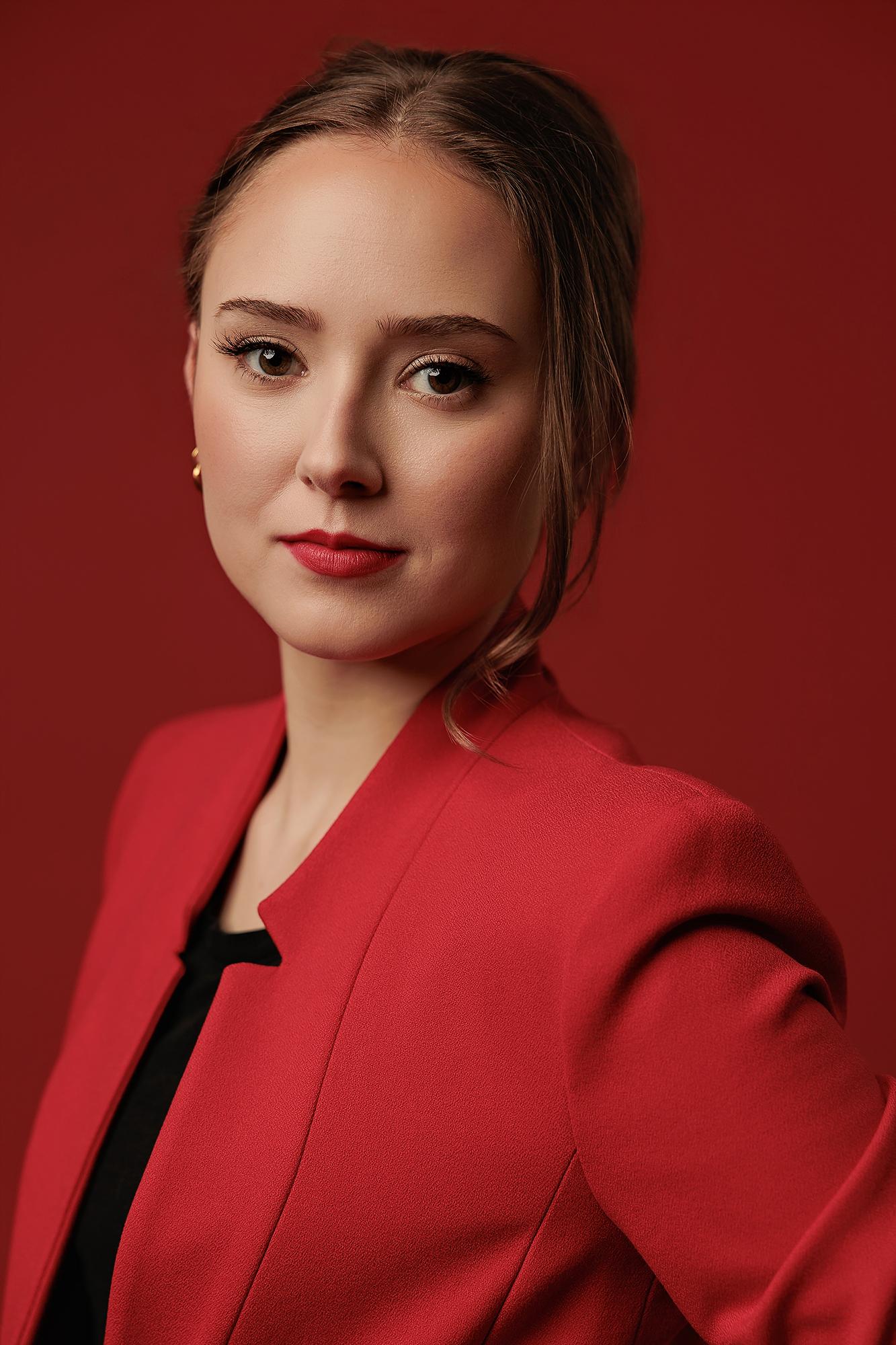 A professional woman in a red blazer poses against a matching backdrop for this Calgary headshot photographer, showcasing a confident and polished look.