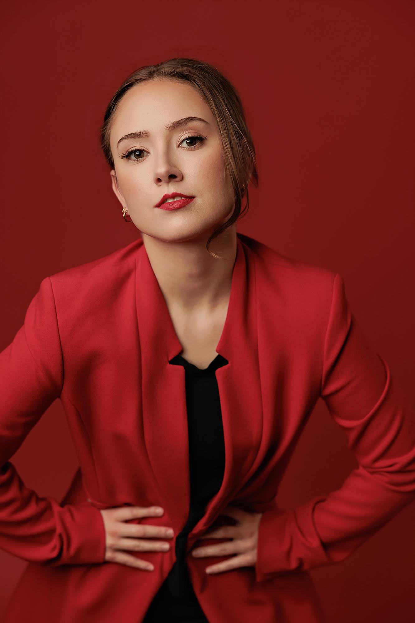 A woman in a vibrant red blazer poses confidently for a professional headshot at our Calgary photography studio, featuring soft lighting and a bold backdrop.