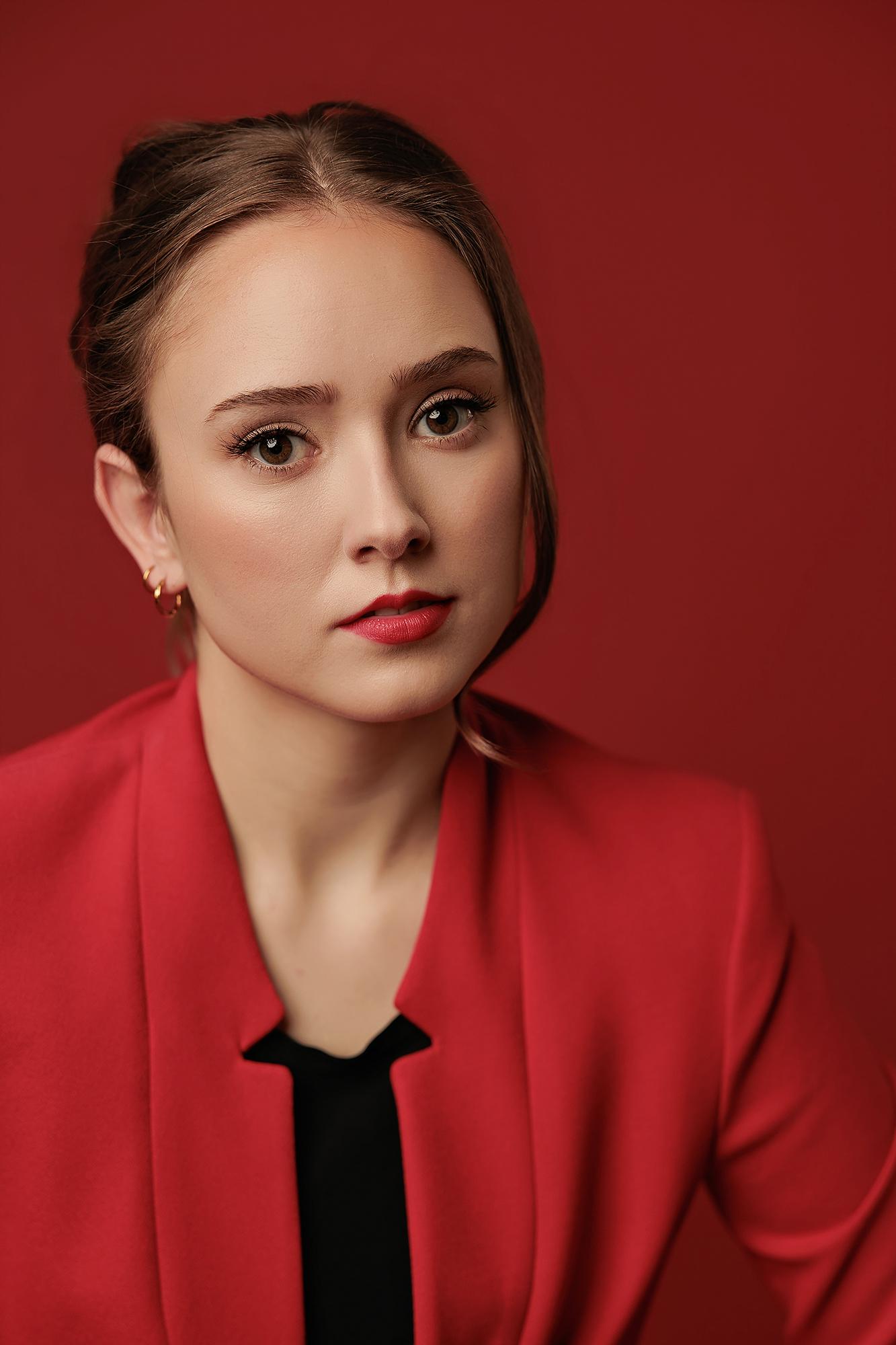 A professional woman in a red blazer poses against a matching backdrop, showcasing the bold personal branding style of our Calgary headshot studio.