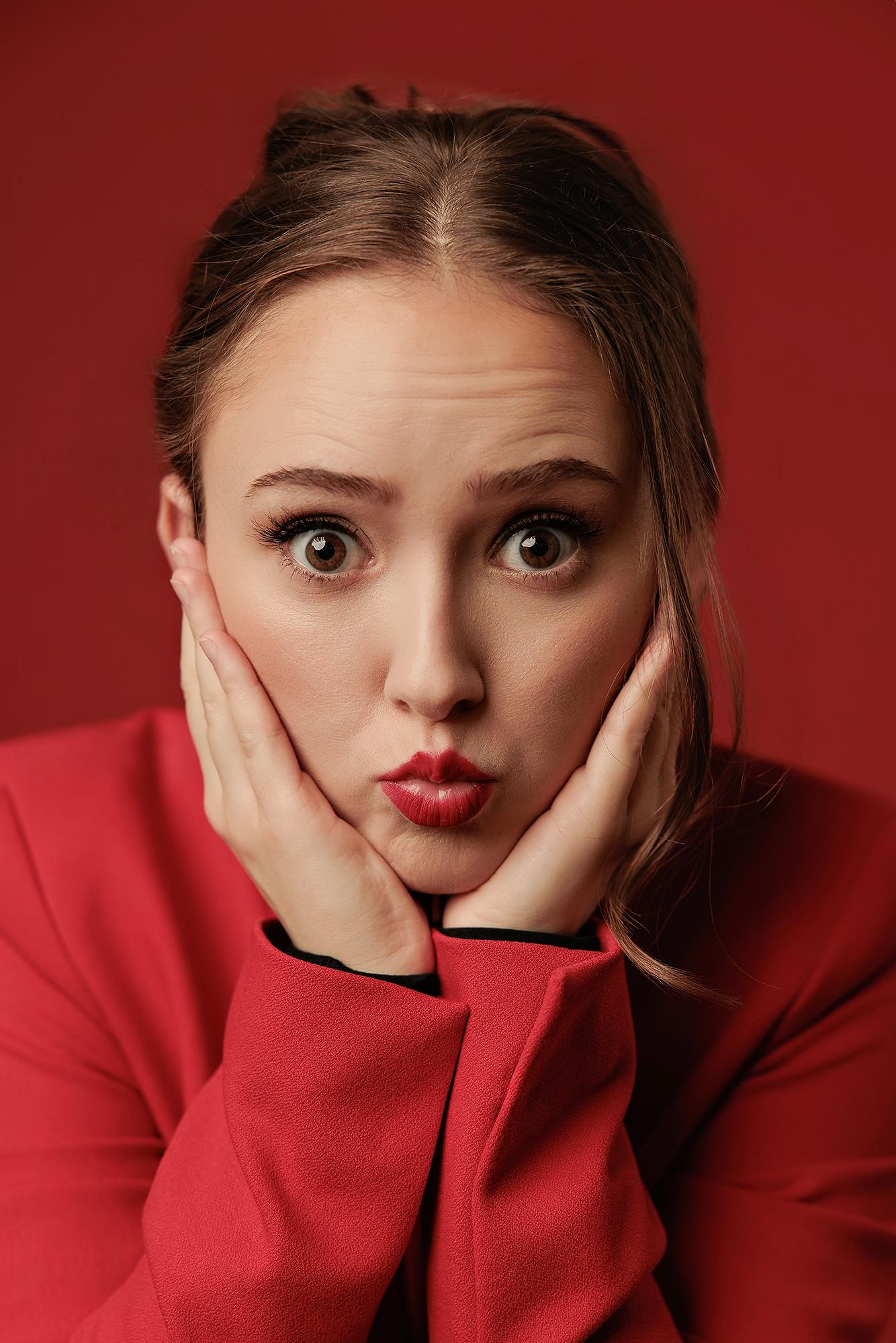 A young woman with expressive eyes and red lipstick poses with hands on her face for this vibrant personal branding session at our Calgary studio.