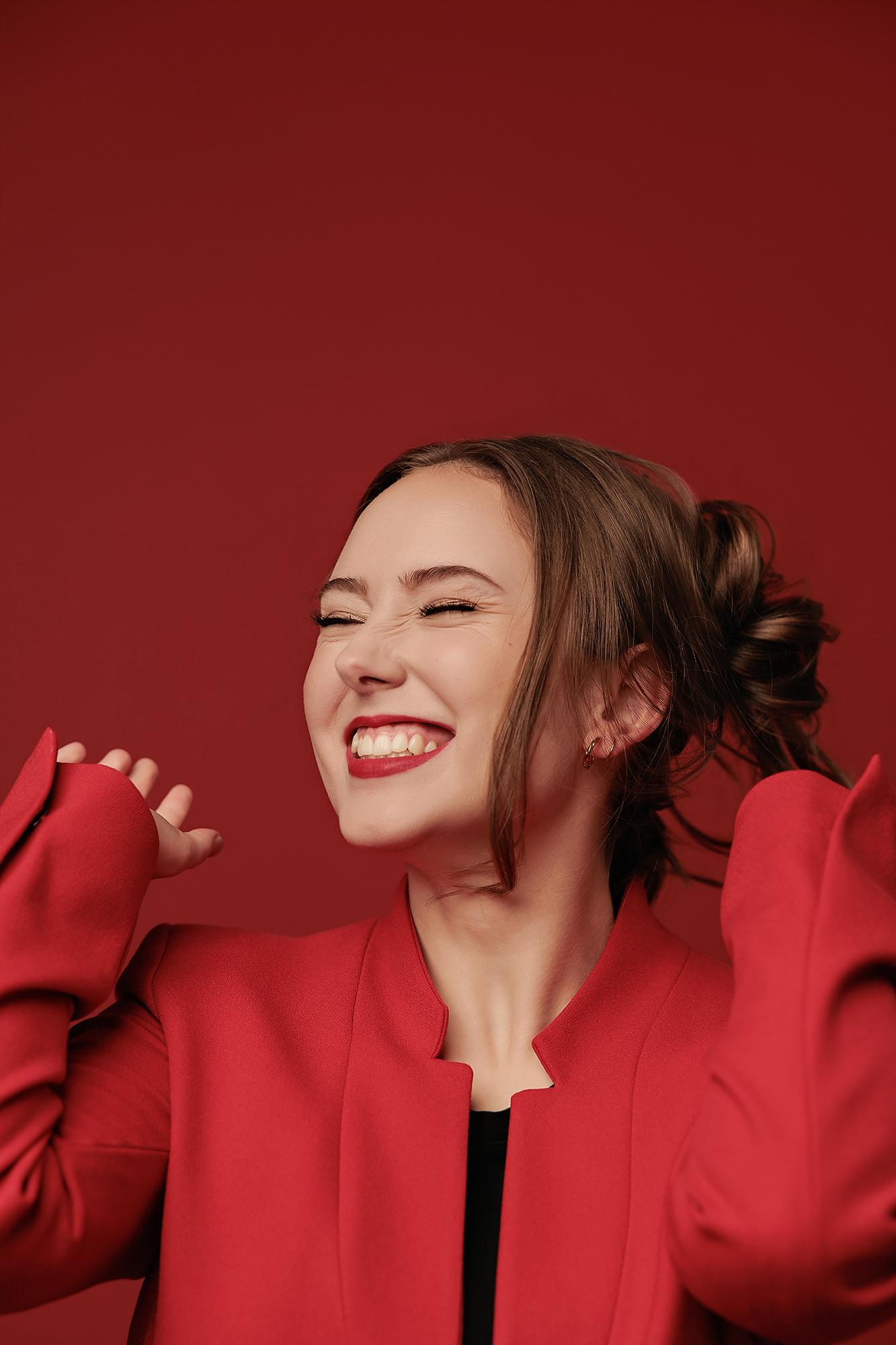 A woman in a vibrant red blazer laughs joyfully against a matching backdrop, showcasing the expressive personal branding style of our Calgary studio.
