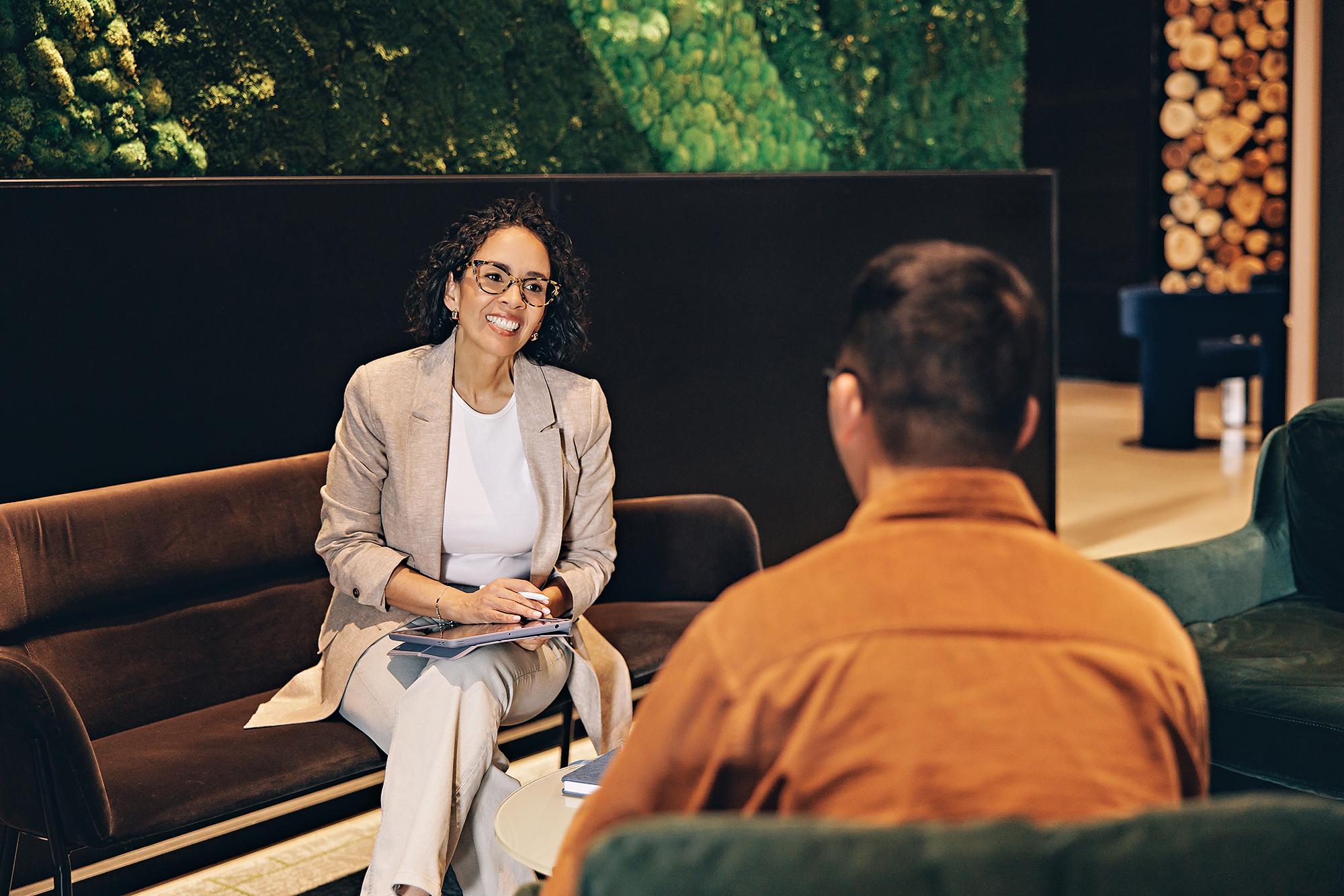 Corporate headshot in Calgary: Businesswoman in a beige blazer meeting with a colleague against a green moss wall