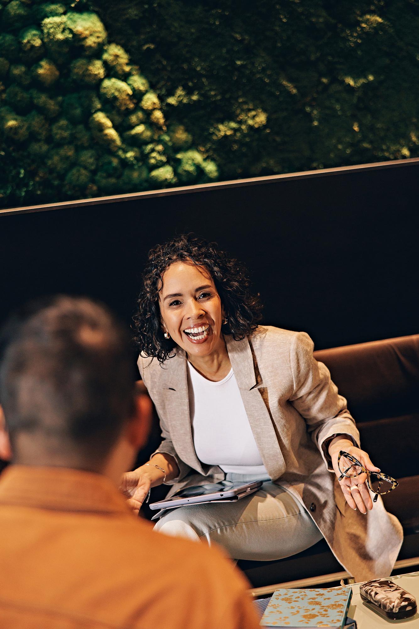 Modern Calgary personal branding: Joyful business woman holding glasses and laughing on a dark lounge couch