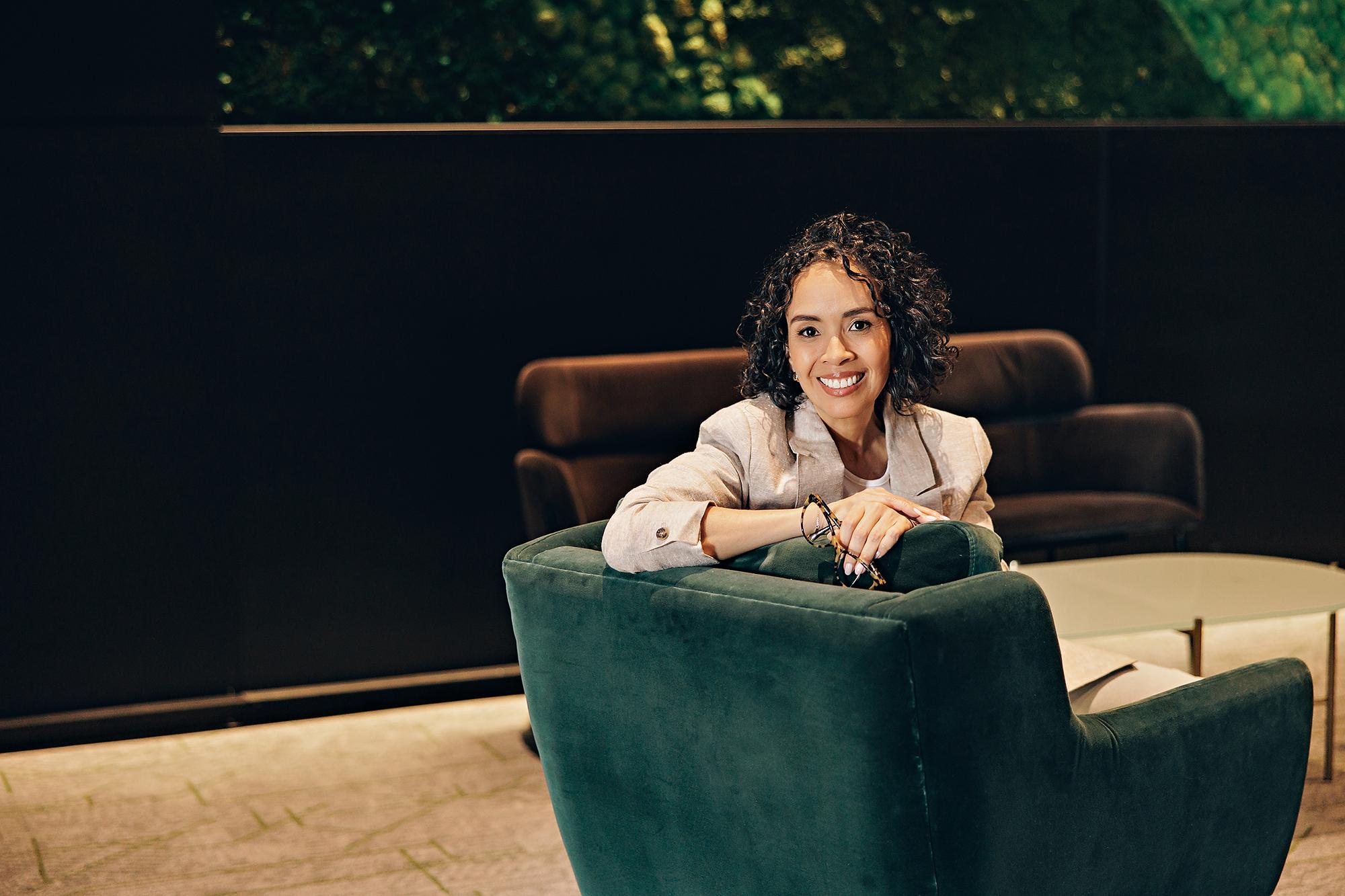 Personal Branding in Calgary: Smiling woman in a beige blazer posing confidently on a green velvet armchair