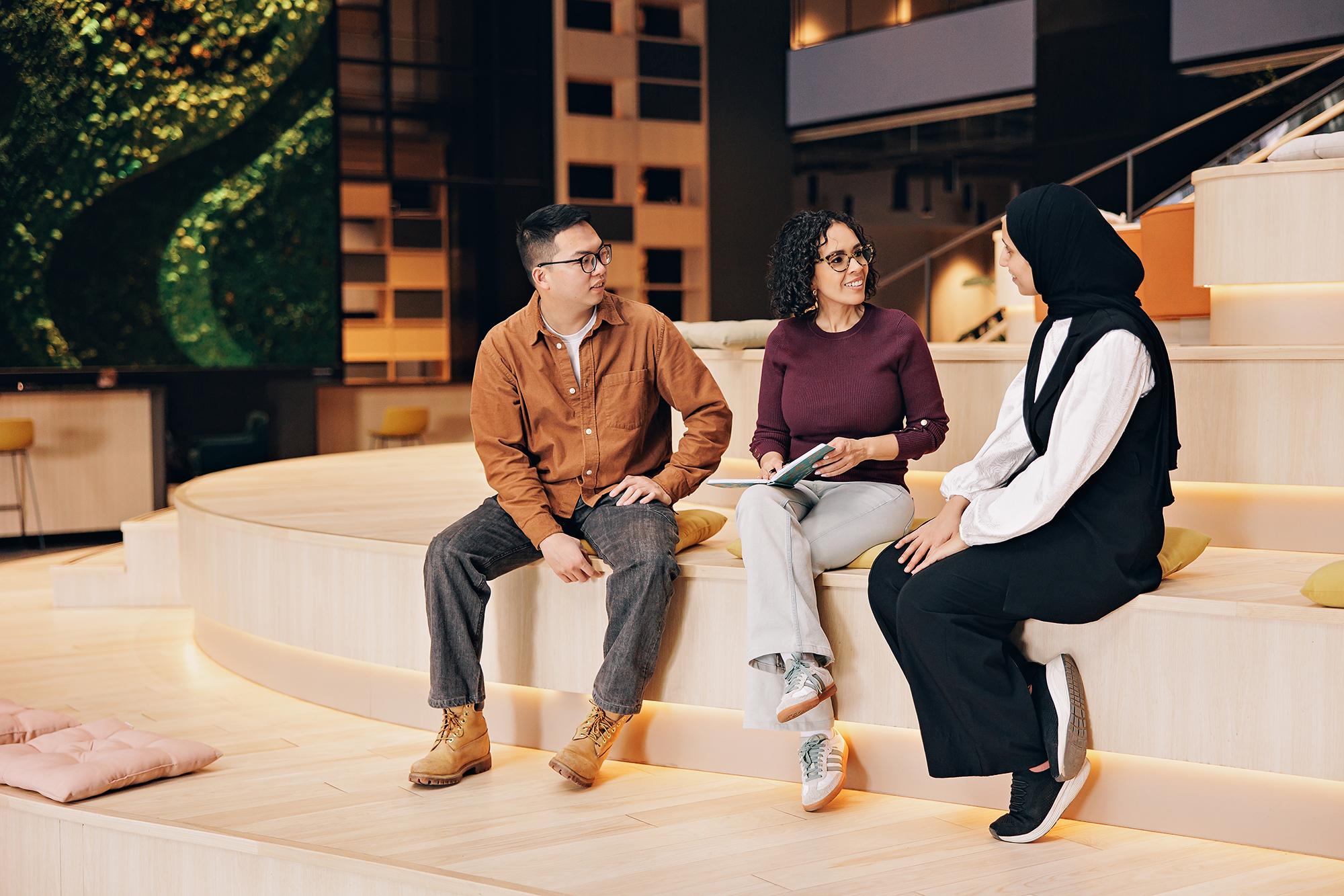 Team headshots Calgary: Diverse group of three business professionals having a collaborative discussion on wooden tiered seating in a modern office