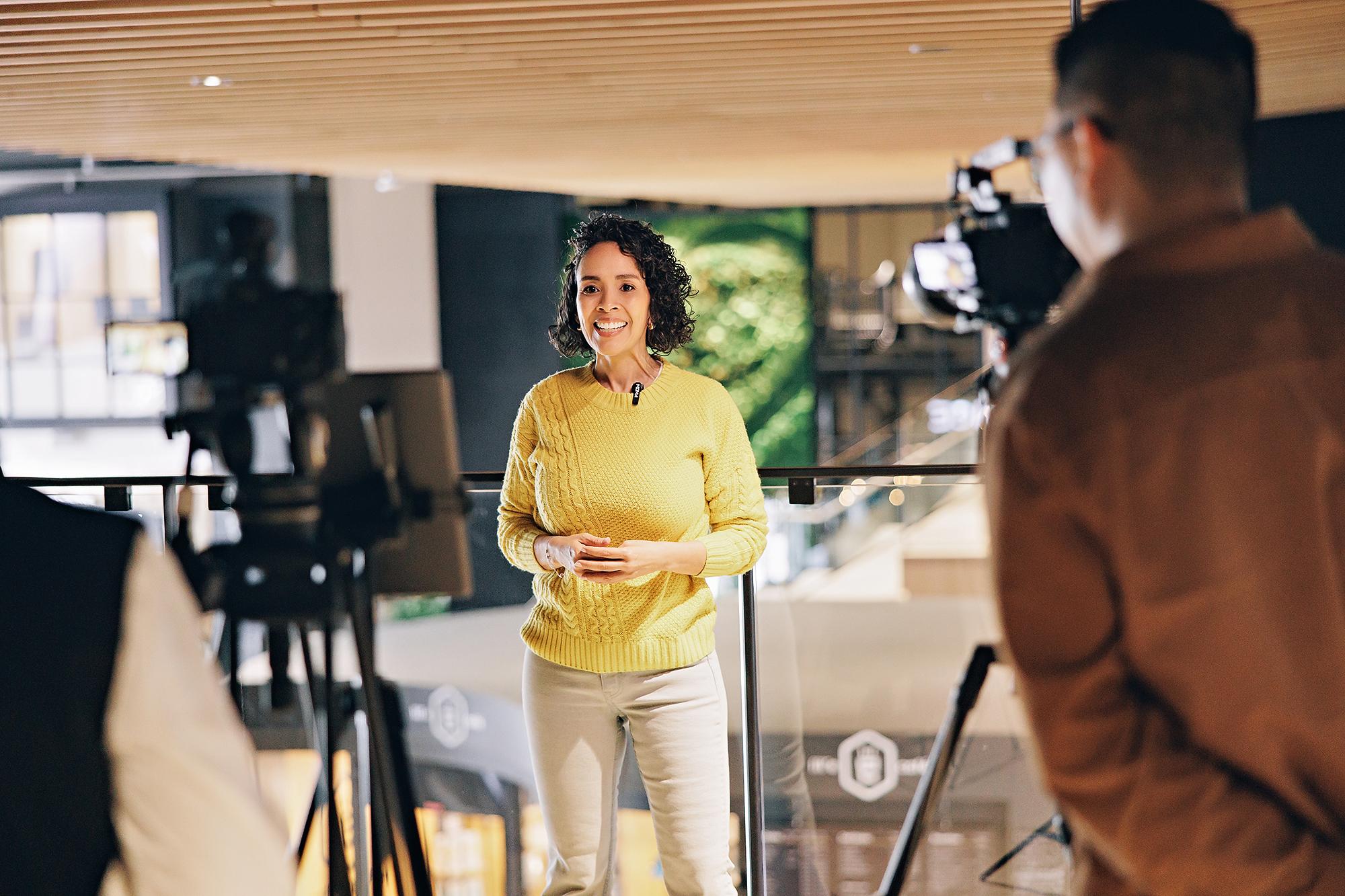 Personal branding photography in Calgary: Woman in a yellow sweater speaking on camera in a modern workspace