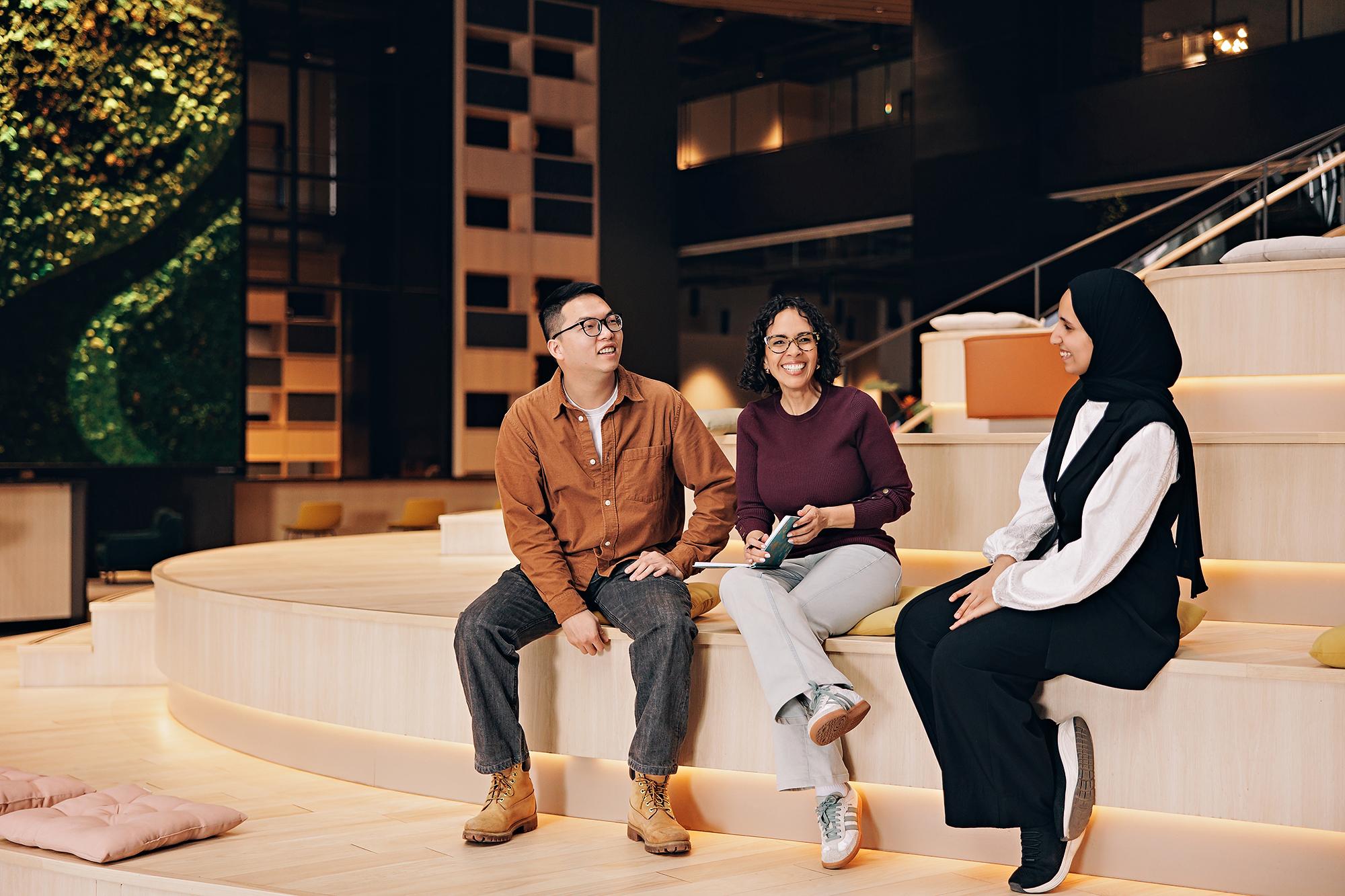 Corporate lifestyle photography Calgary: Three colleagues, including a woman in a hijab, smiling and chatting during an informal meeting on wooden office steps