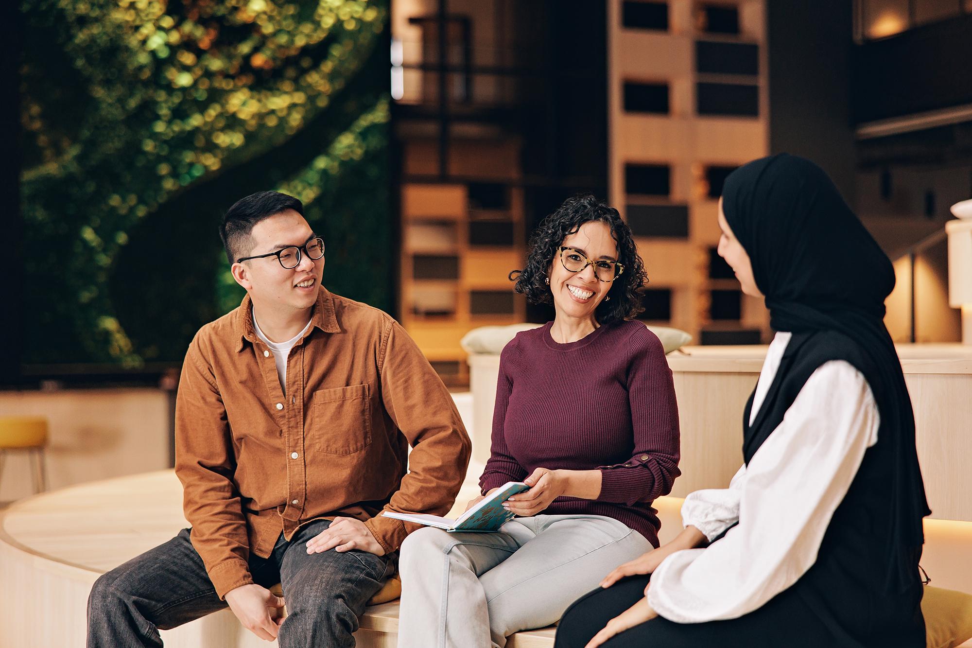 Calgary business branding photography: Female executive in a burgundy sweater smiling at the camera while sitting with two team members in a contemporary workspace