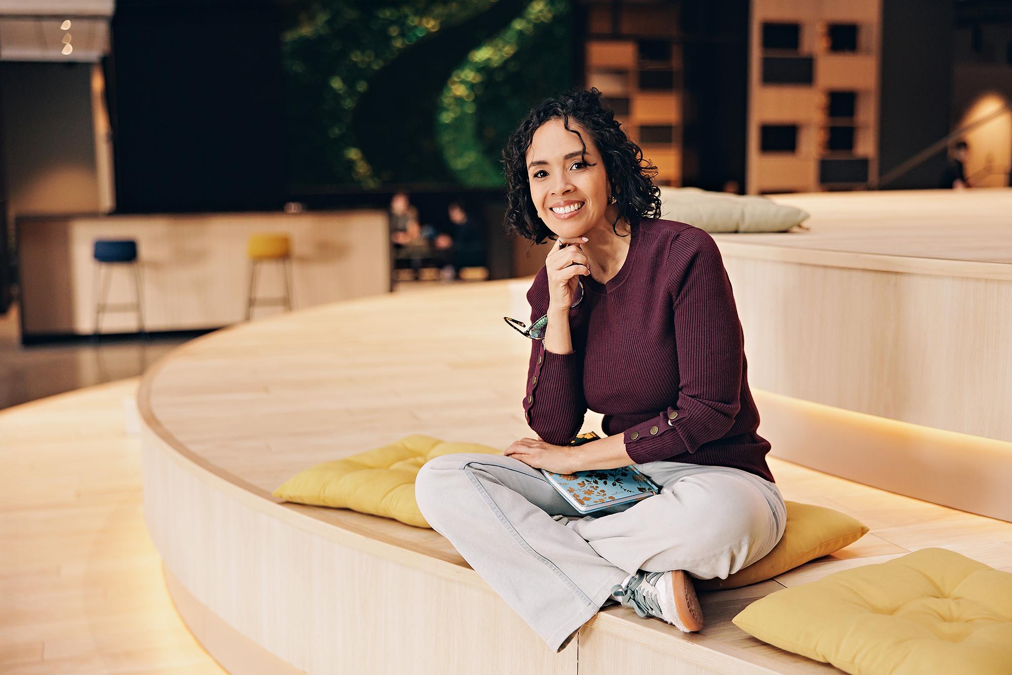 Professional lifestyle headshots in Calgary: Businesswoman in a burgundy sweater smiling at the camera in a modern workspace