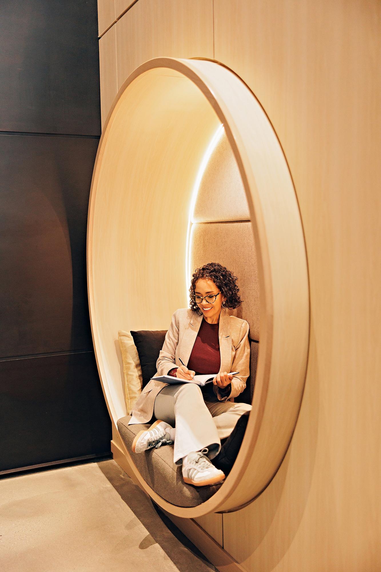 Calgary corporate lifestyle headshots: Female professional wearing glasses sitting in a modern circular wall alcove, writing in a blue notebook