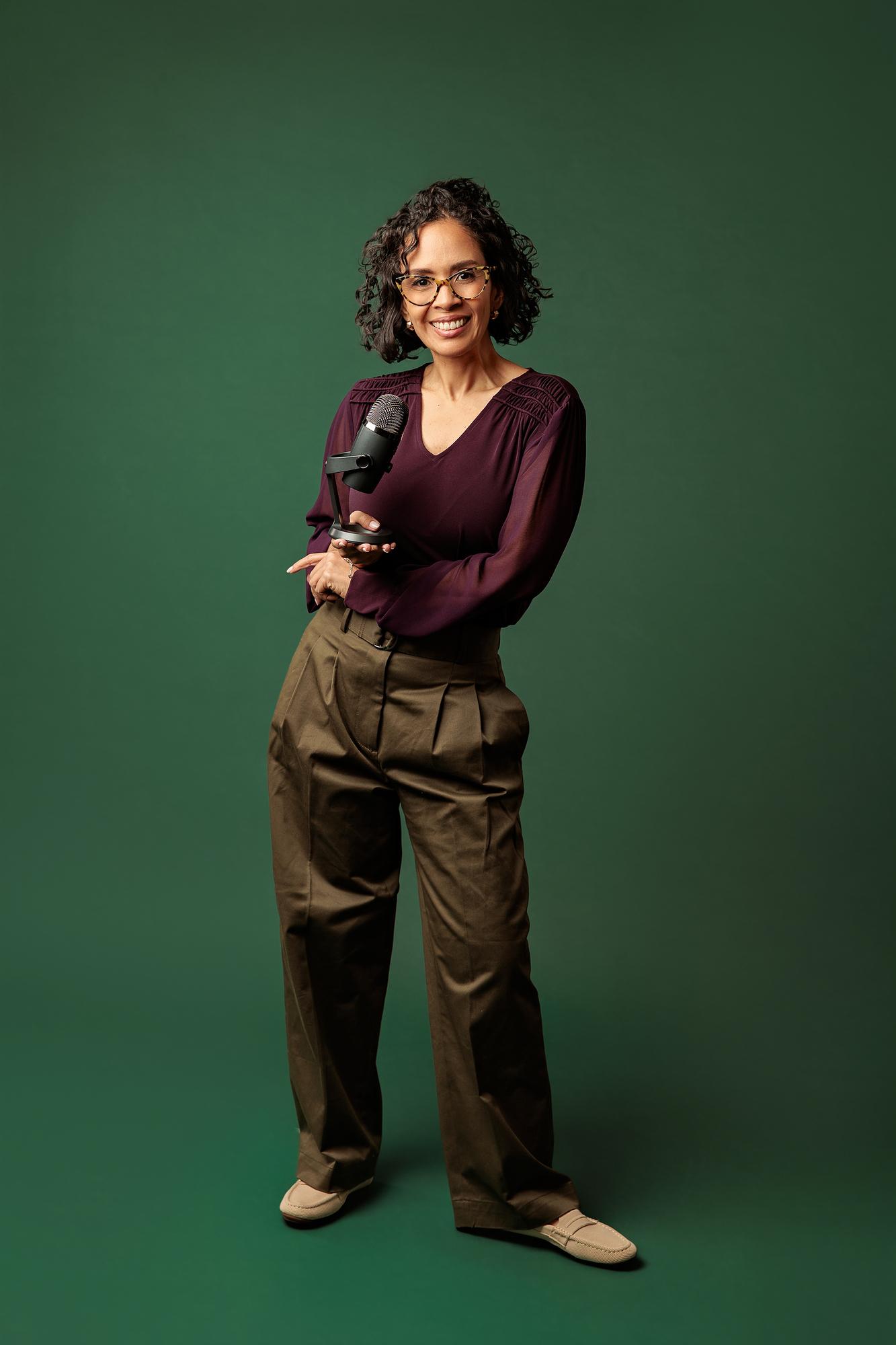 Personal brand photography Calgary studio: Female entrepreneur standing and holding a podcast microphone against a solid dark green backdrop