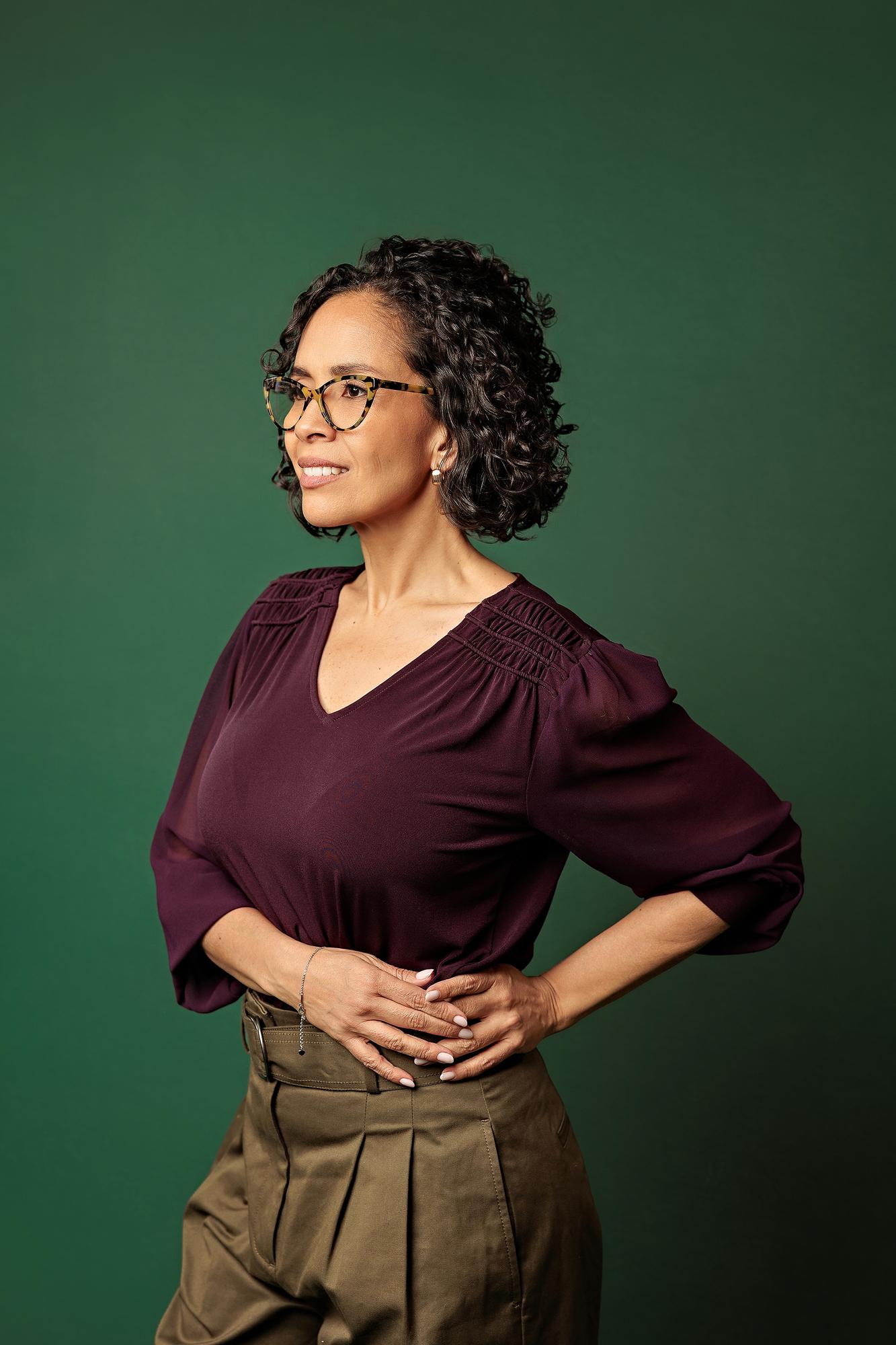 Personal branding Calgary lifestyle session: Professional woman with glasses standing with hands on her hips against a dark green studio backdrop