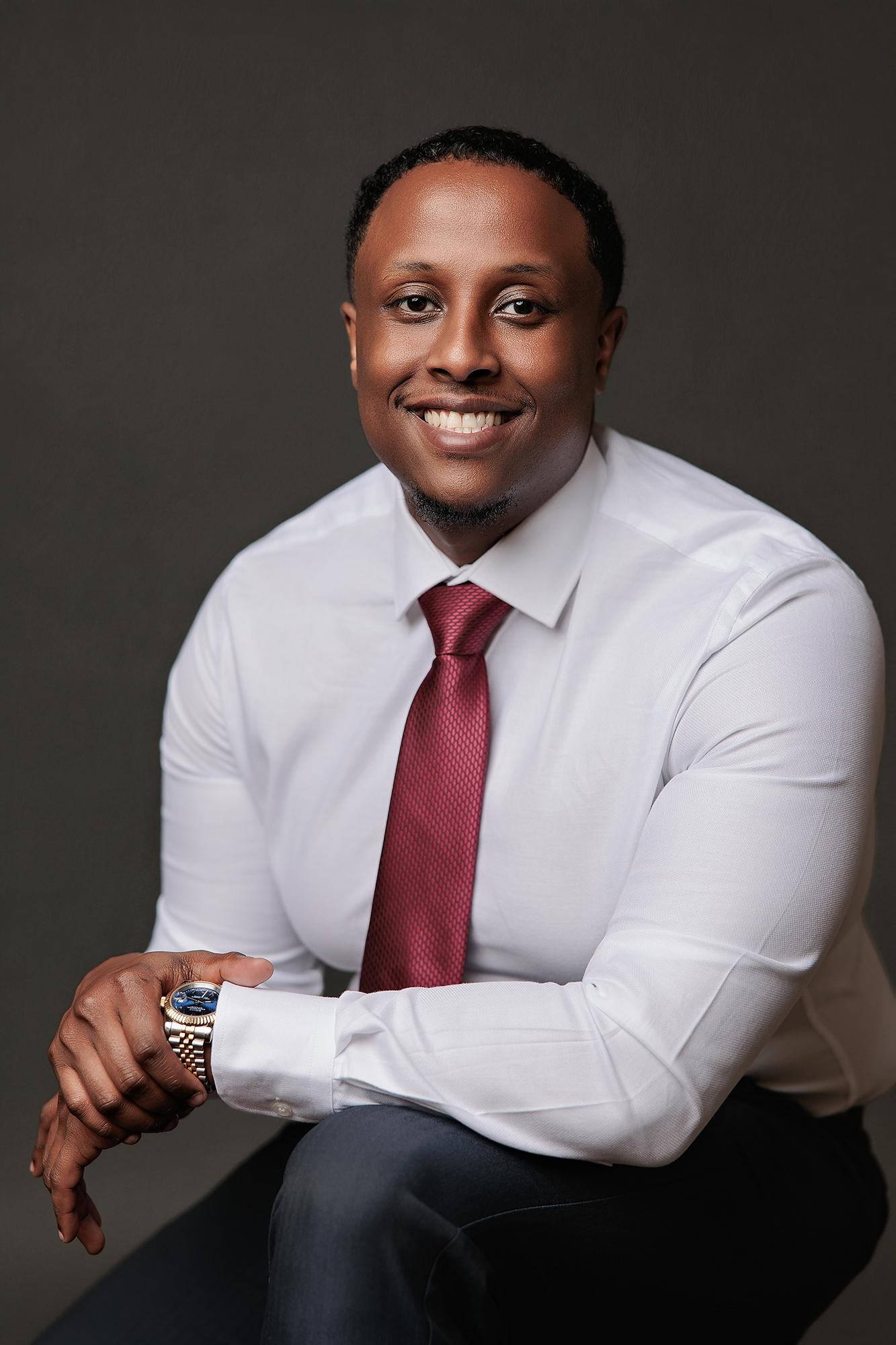 A smiling man in a white dress shirt and maroon tie poses for a professional headshot at a Calgary photography studio with soft, flattering lighting.