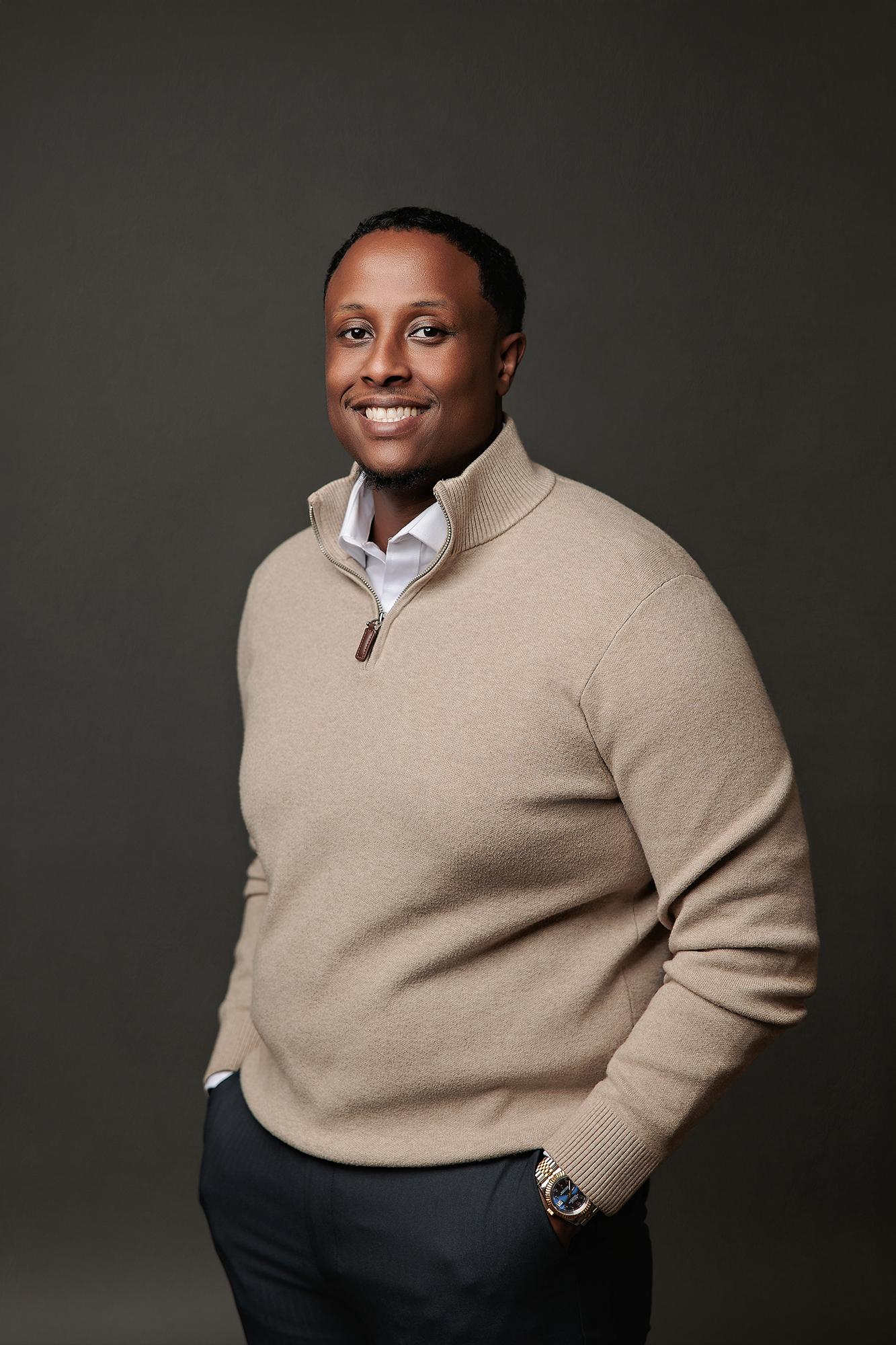 A smiling man in a beige quarter-zip sweater poses for a professional headshot at our Calgary photography studio, featuring soft studio lighting.