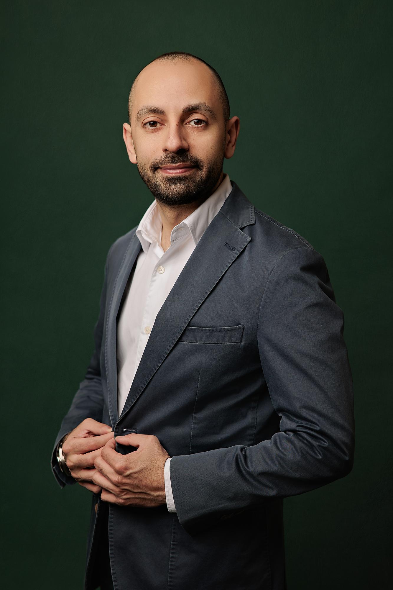 A confident man in a dark blazer and white shirt subtly smiles while adjusting his jacket, a professional headshot from a Calgary photography studio.