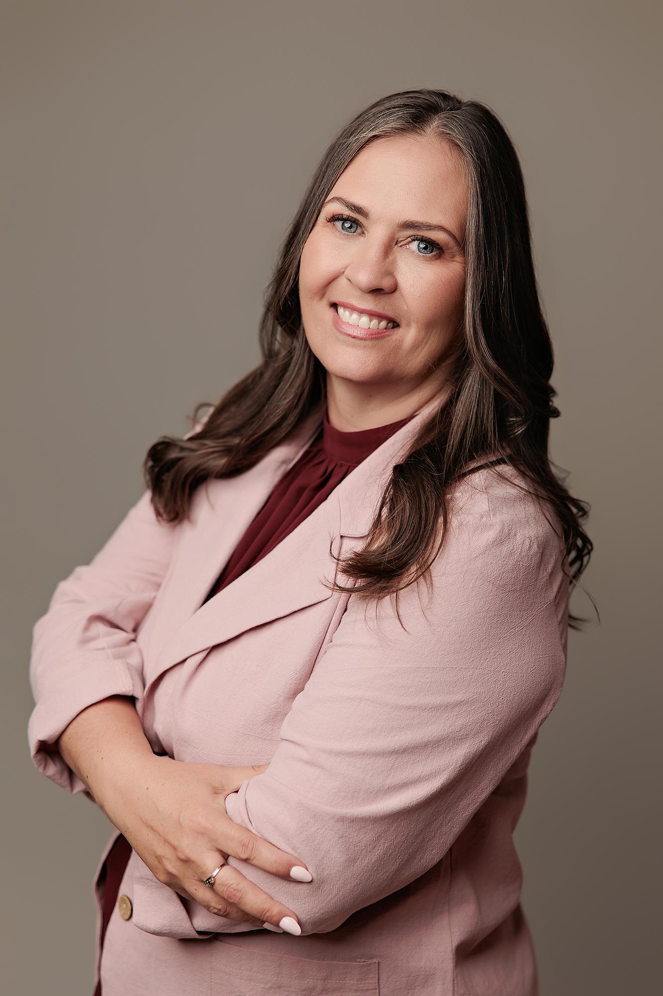 A professional woman smiles confidently in a pink blazer at our Calgary headshot studio, captured with soft, flattering lighting and a neutral background.