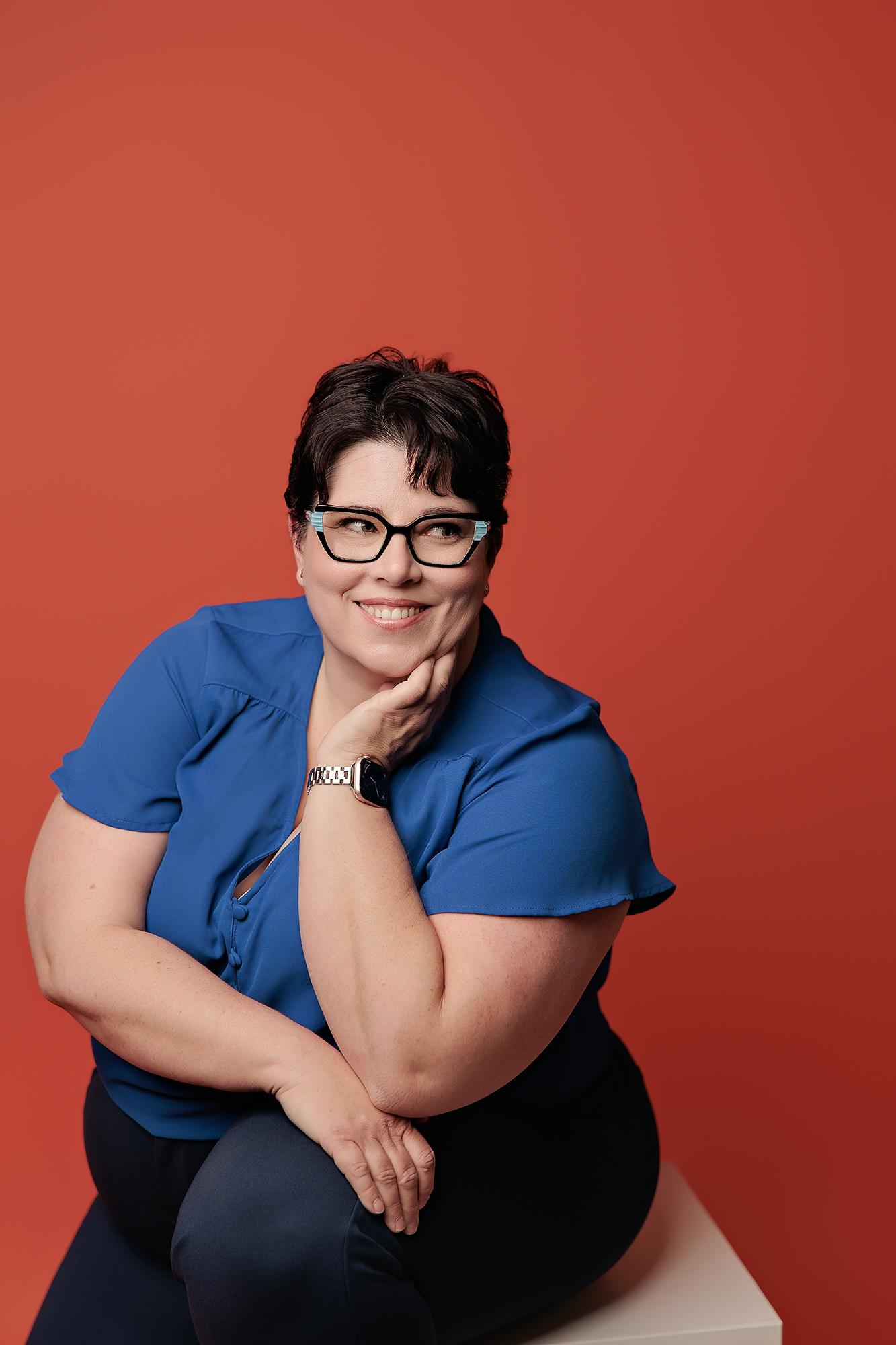A smiling woman in a blue blouse poses for a professional headshot at our Calgary photography studio, featuring bright lighting against a bold red backdrop.