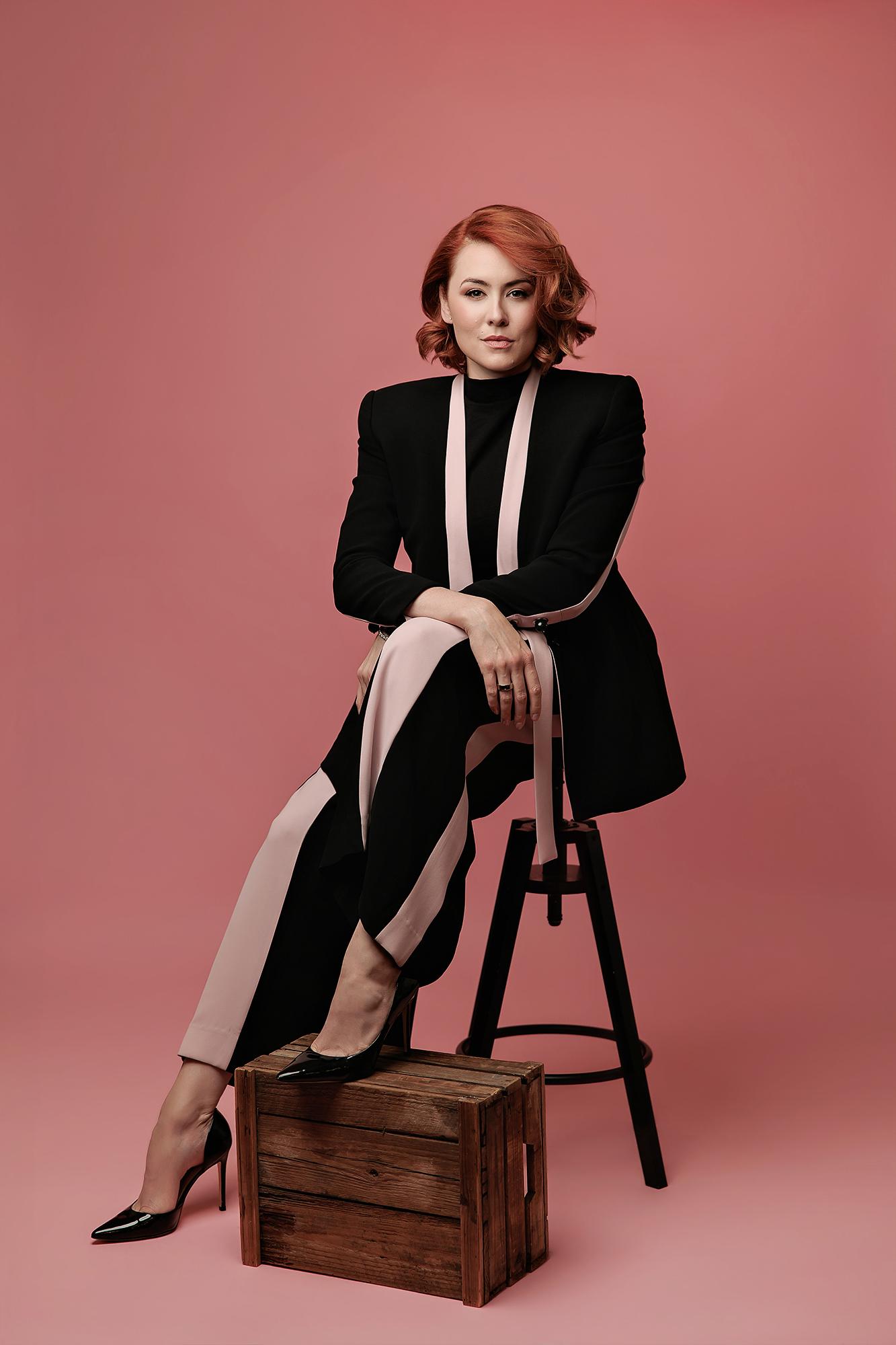 A woman with auburn hair wears a modern black and pink suit in this professional Calgary studio headshot, captured with confident lighting.