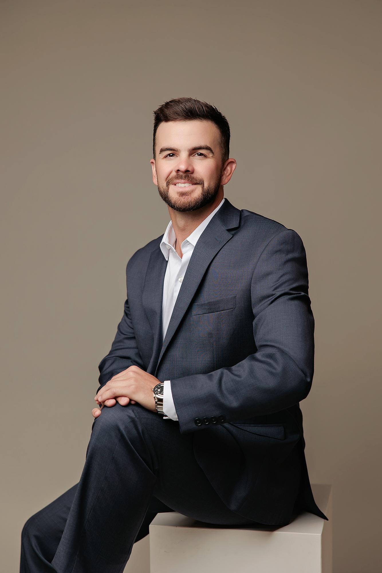 A professional man in a navy suit smiles confidently during a session at our Calgary headshot studio, featuring soft studio lighting and a neutral backdrop.
