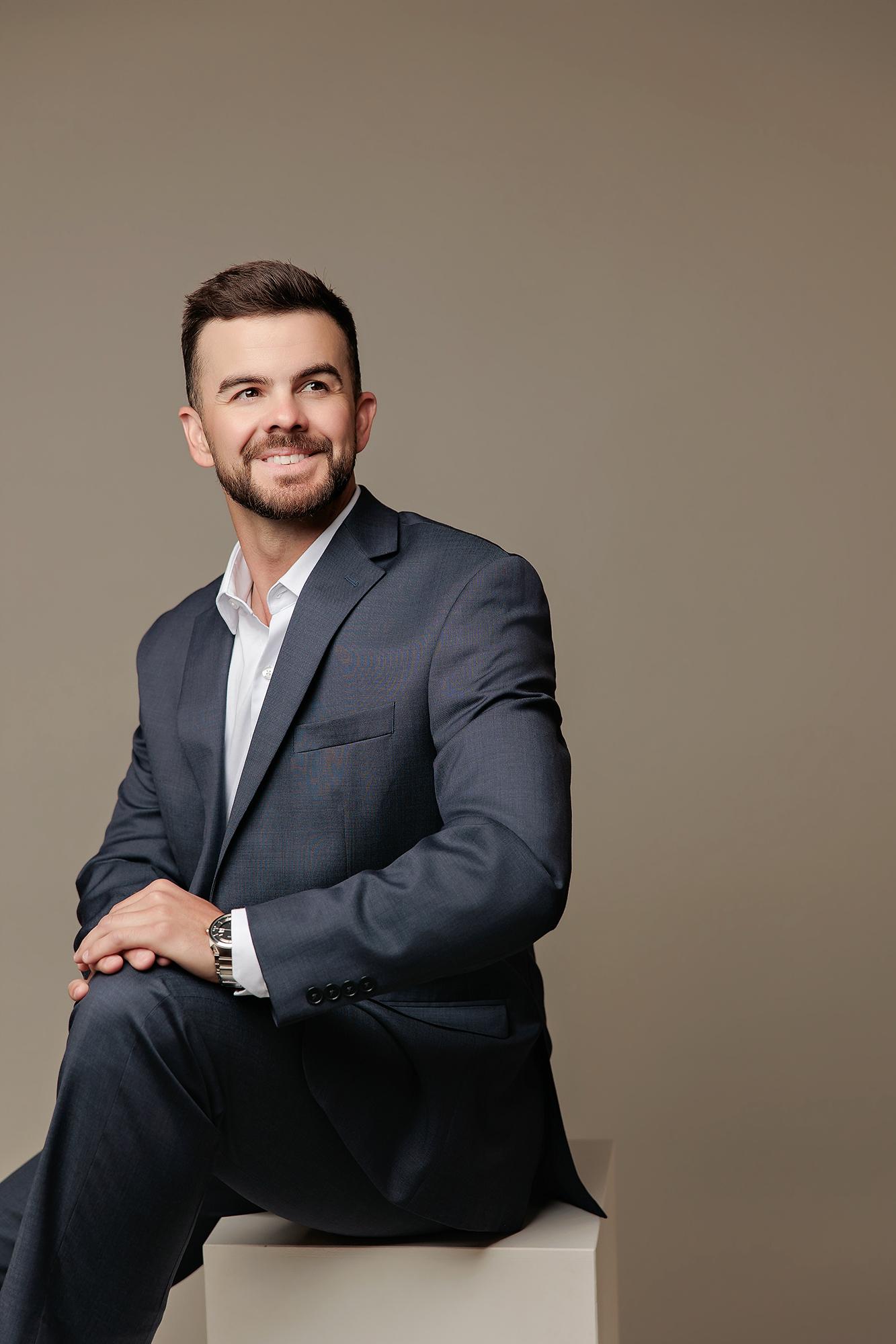 A smiling man in a navy suit poses for a professional headshot at our Calgary photography studio, featuring soft lighting against a neutral backdrop.