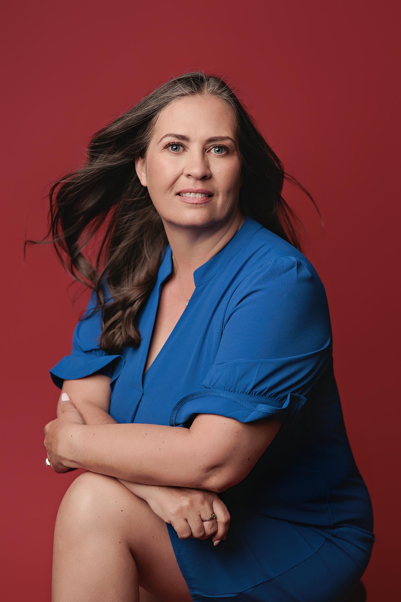 A woman with flowing dark hair wears a vibrant blue dress against a bold red background, captured by a Calgary headshot photographer for personal branding.