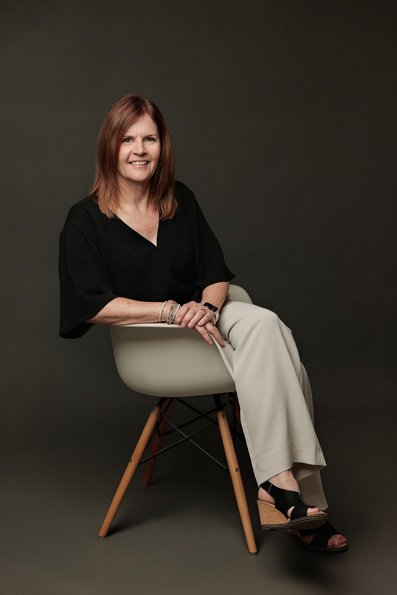 A woman with auburn hair smiles warmly in a professional Calgary studio, wearing a black top and light trousers for a polished personal branding portrait.