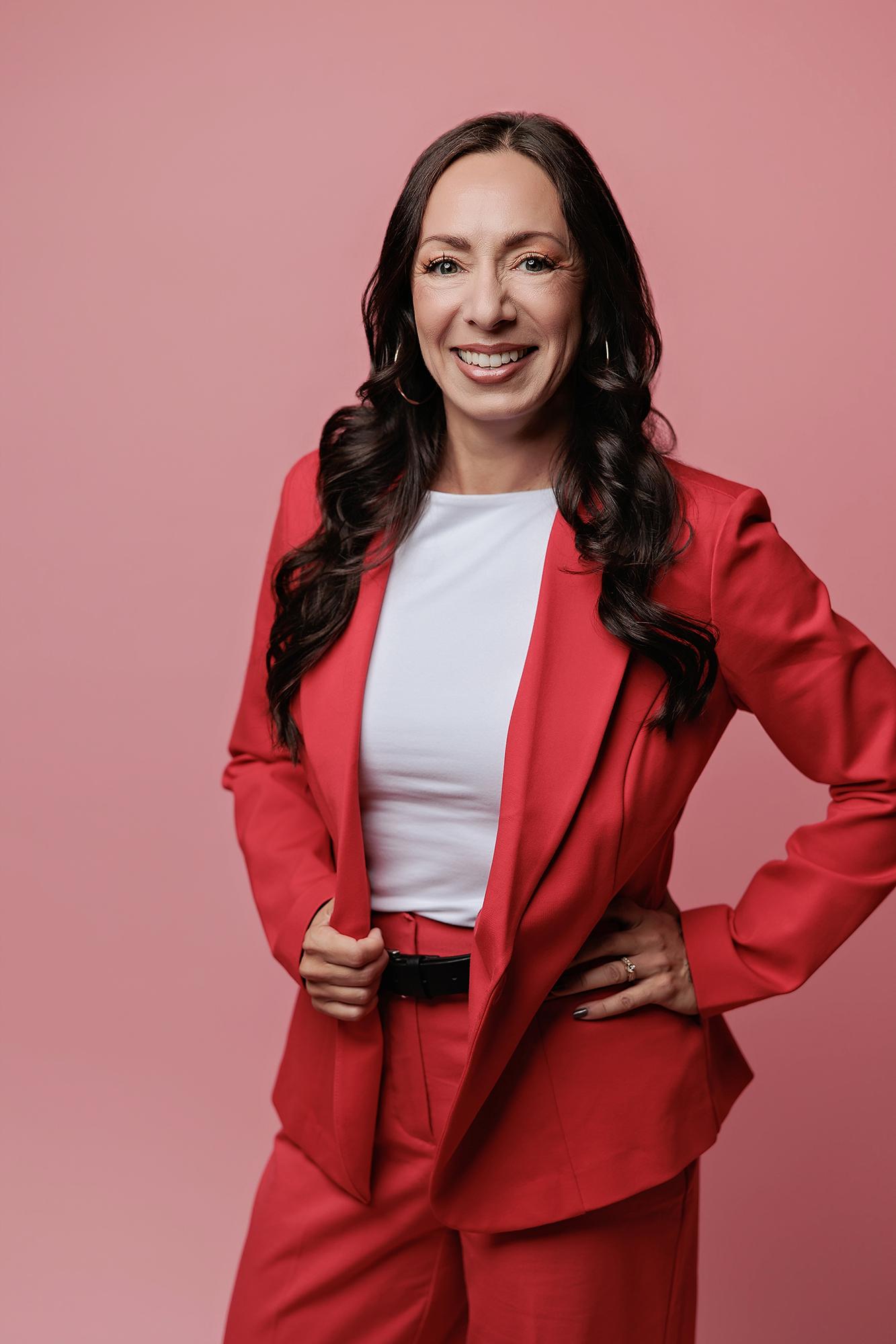 A woman with long dark hair smiles confidently in a vibrant red suit, showcasing the professional branding style of our Calgary photography studio.