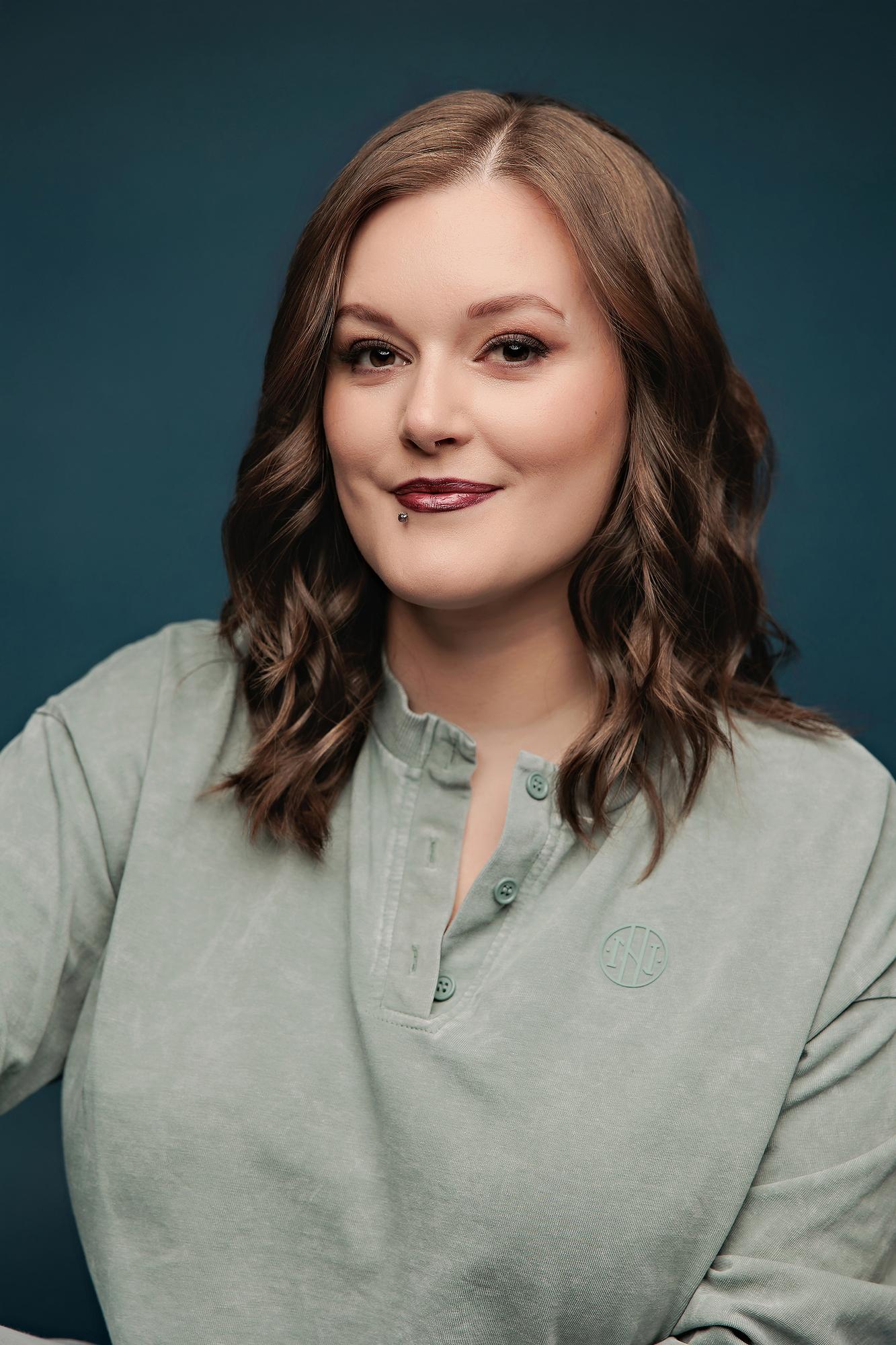 Personal branding headshot Calgary: Close-up portrait of a young woman in a sage green henley with wavy hair and bold lip against a teal studio background