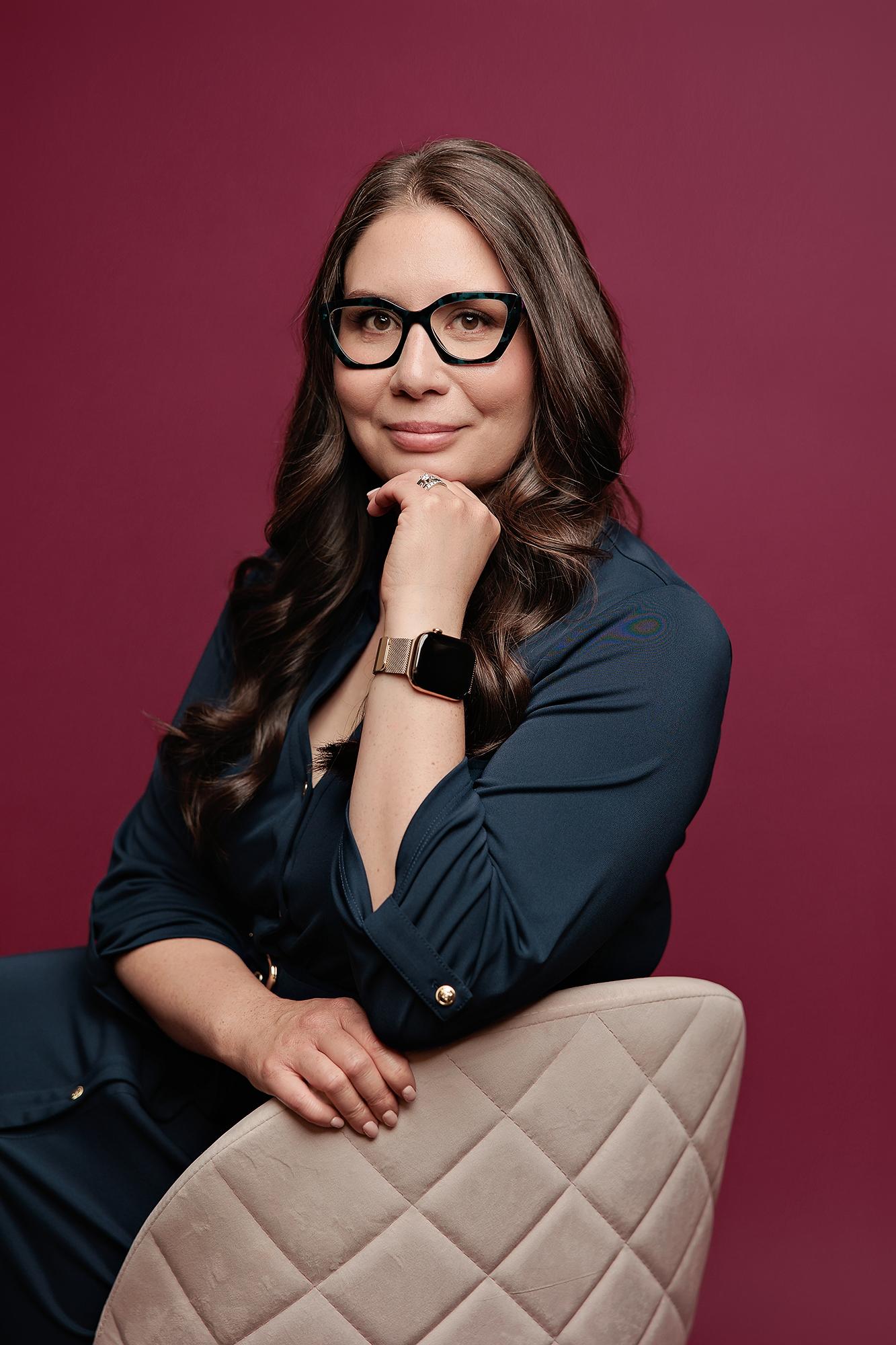 A woman in a navy dress poses for a professional headshot in our Calgary studio, featuring soft studio lighting against a bold, deep red backdrop.