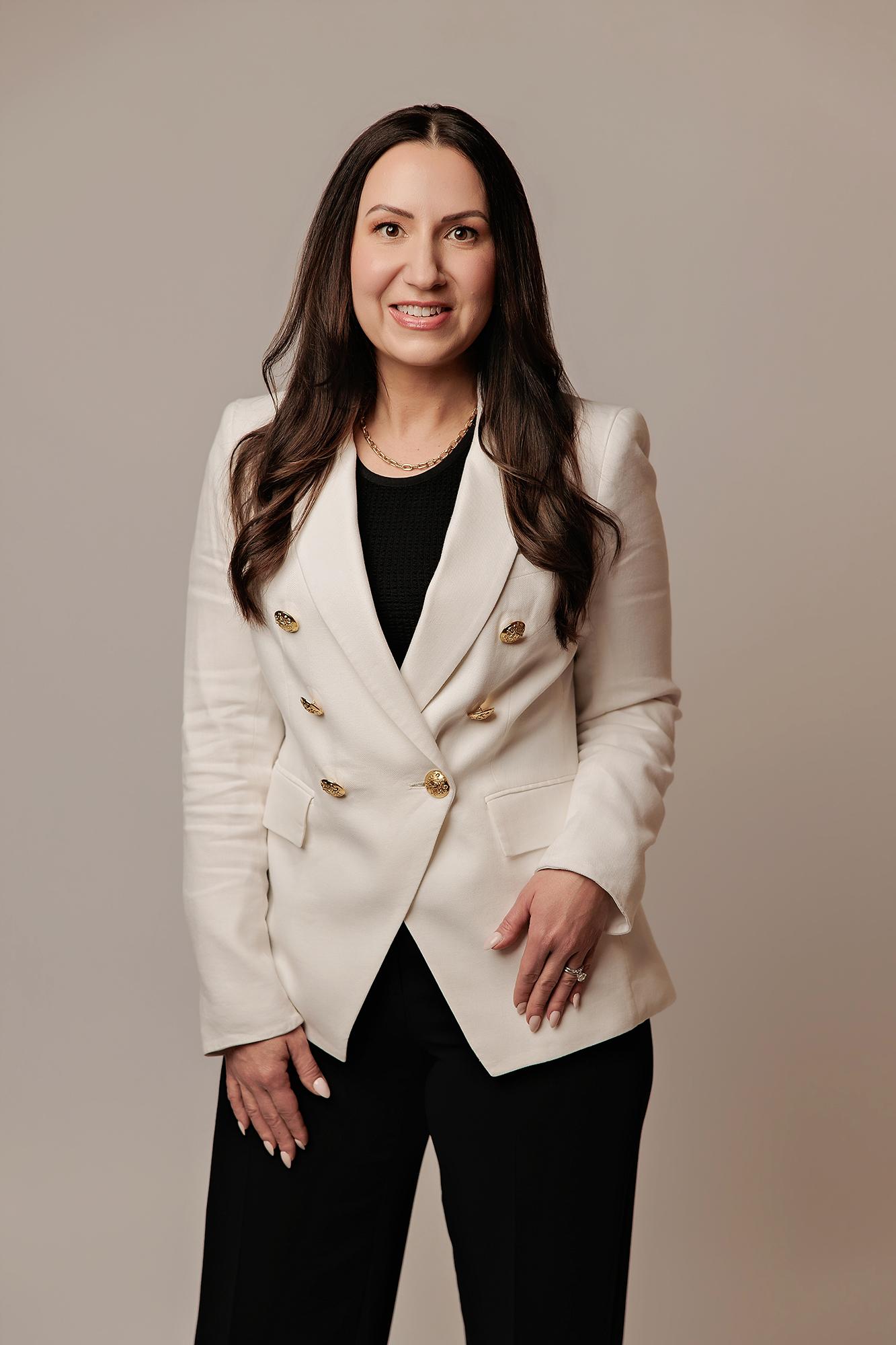 A smiling woman in a white blazer poses for a professional headshot at our Calgary photography studio, featuring soft studio lighting on a neutral backdrop.