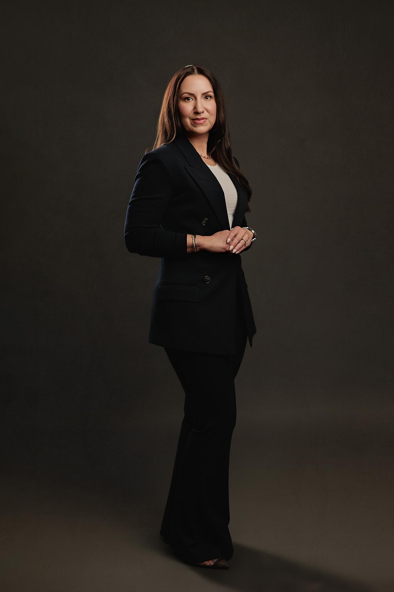 A confident woman in a black blazer poses for a professional headshot at our Calgary photography studio, featuring soft studio lighting on a dark backdrop.