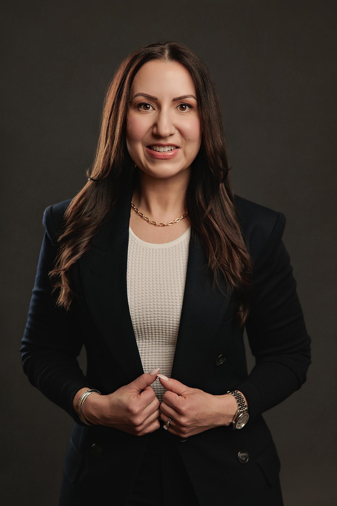 A woman with long dark hair smiles in a professional blazer at our Calgary headshot studio, showcasing polished lighting and a modern aesthetic.
