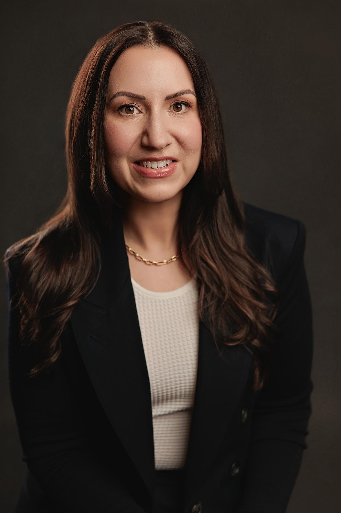 A smiling woman in a black blazer and white top poses for a professional headshot at our Calgary photography studio, featuring soft studio lighting.