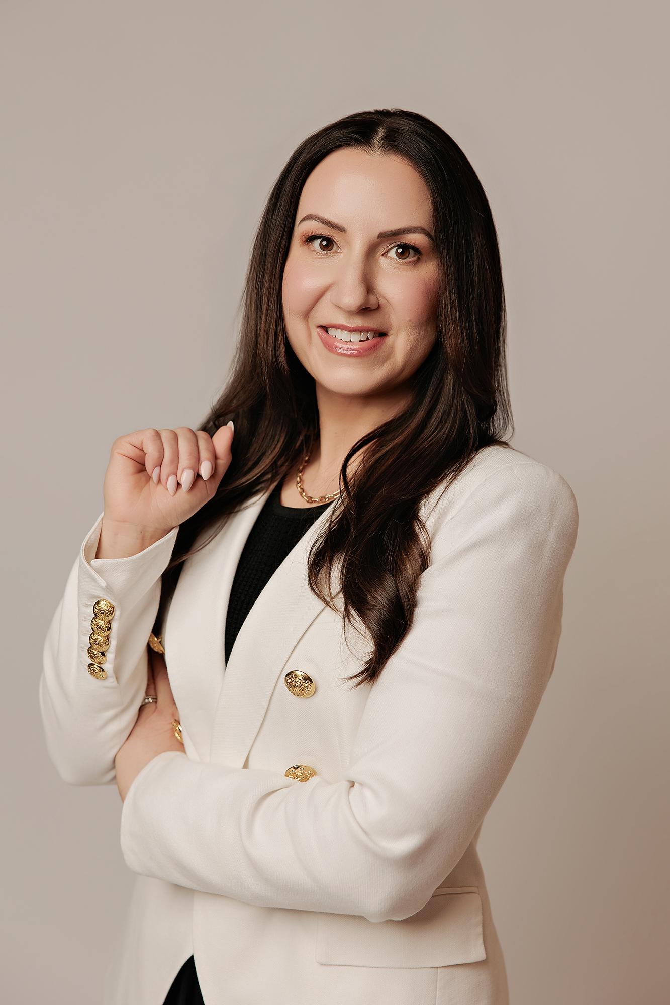 A woman with long dark hair smiles confidently in a white blazer, showcasing the professional quality of our Calgary headshot photography studio.
