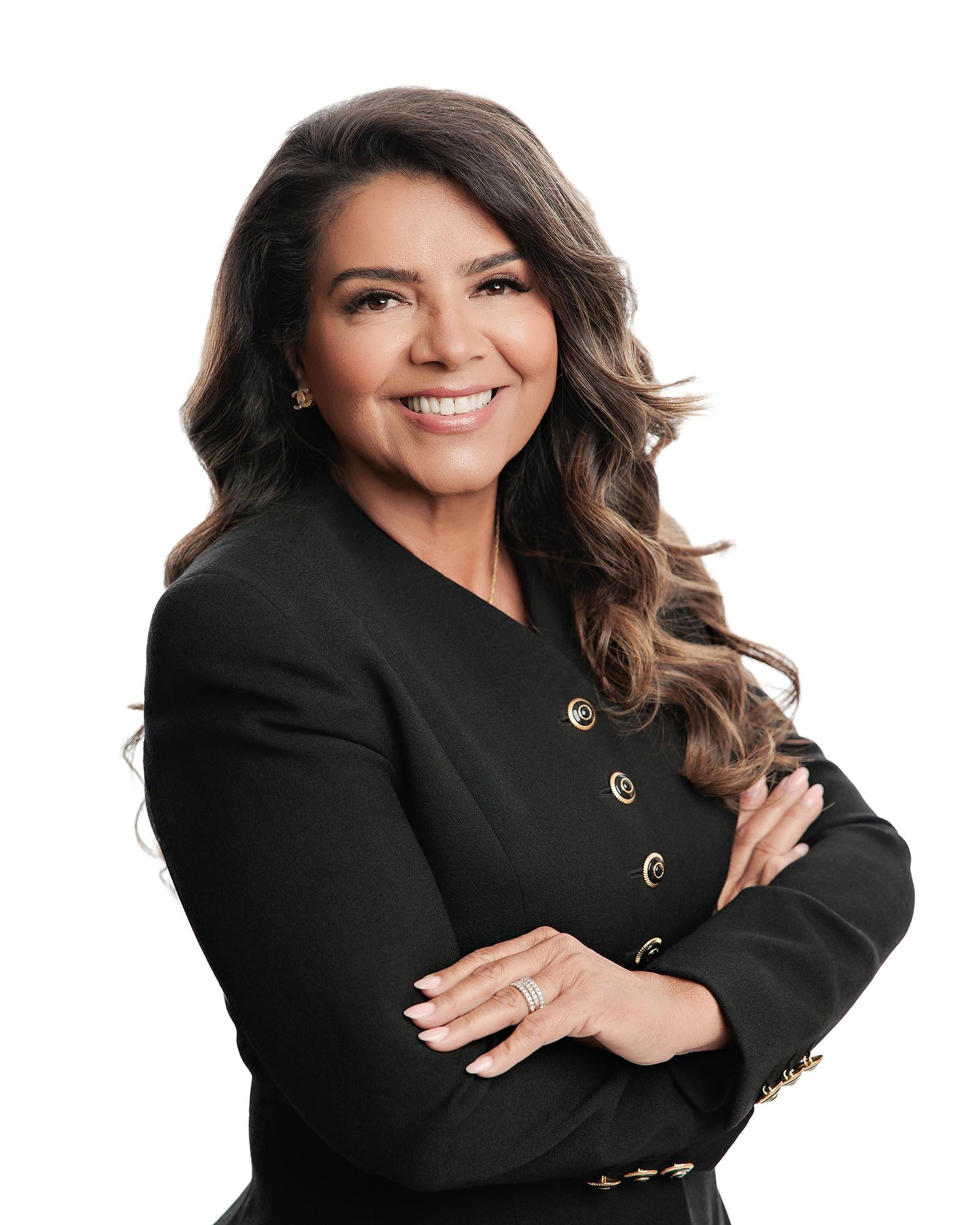 Professional headshot Calgary white background: Confident businesswoman in a black double-breasted blazer with gold hardware standing with arms crossed and a warm smile against a pure white studio background