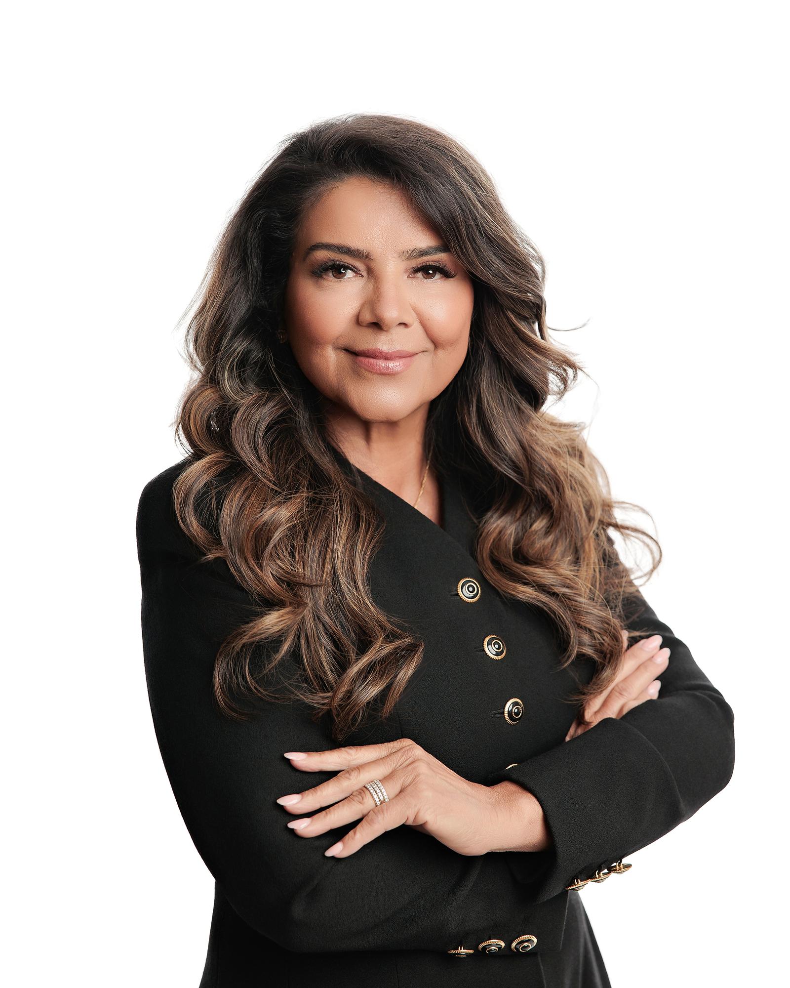 Professional headshot Calgary white background: Poised businesswoman in a black double-breasted blazer with gold hardware standing with arms crossed and a composed expression against a pure white studio background