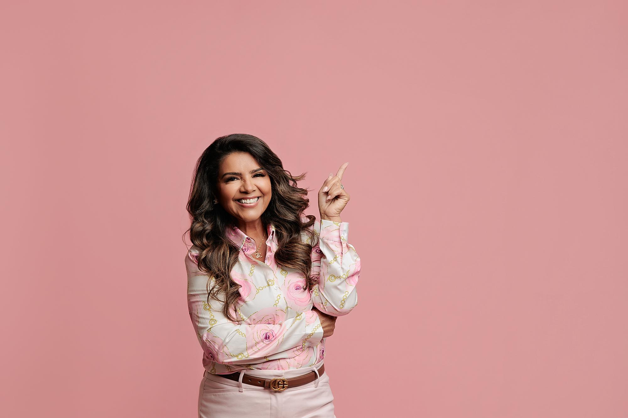Personal branding photography Calgary studio: Professional woman in a pink floral blouse holding a name and phone number sign, smiling warmly at camera against a pink background