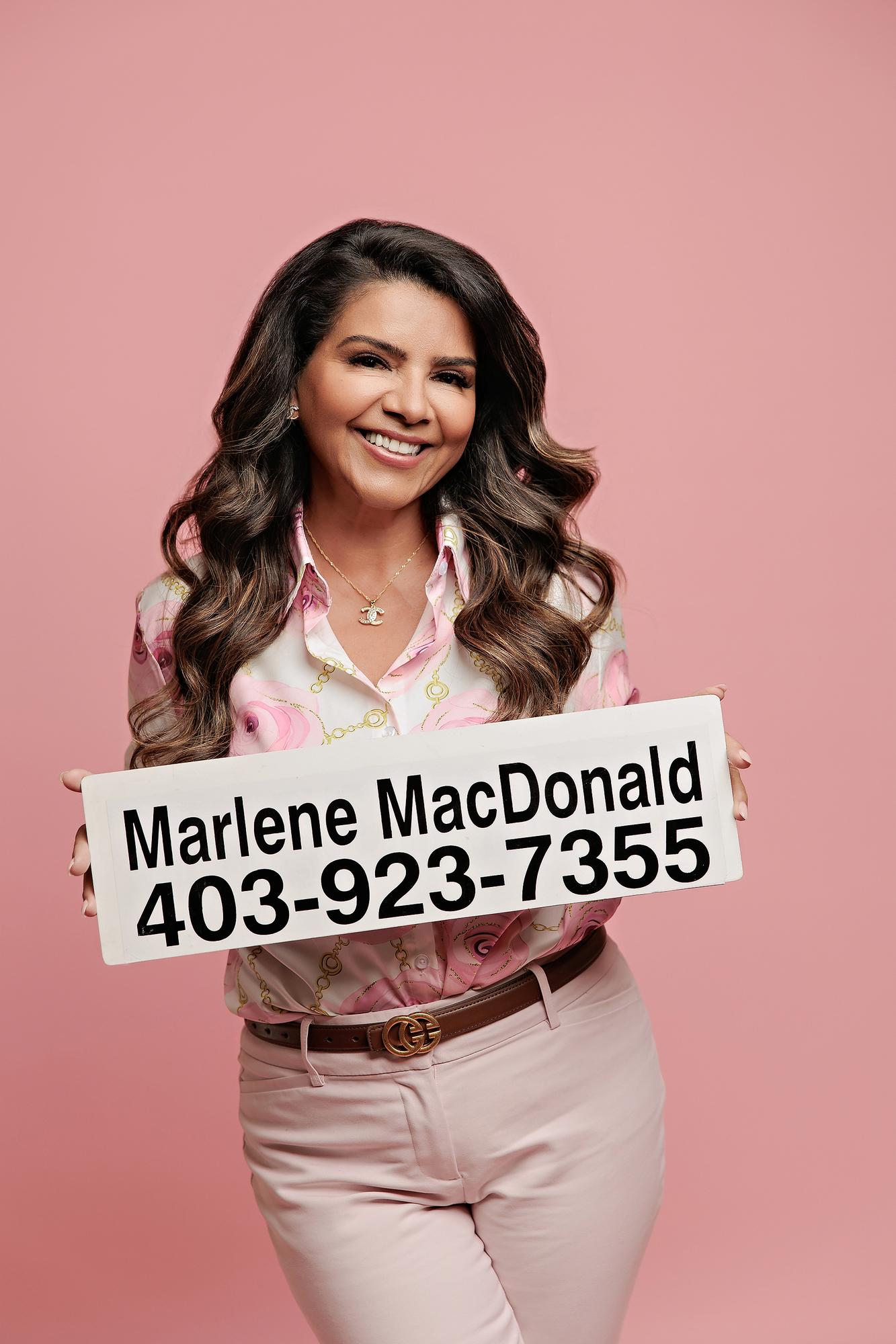 Calgary personal branding session: Confident businesswoman in a blue blazer and jeans seated relaxed on a white studio cube with hands resting on knee, warm grey background